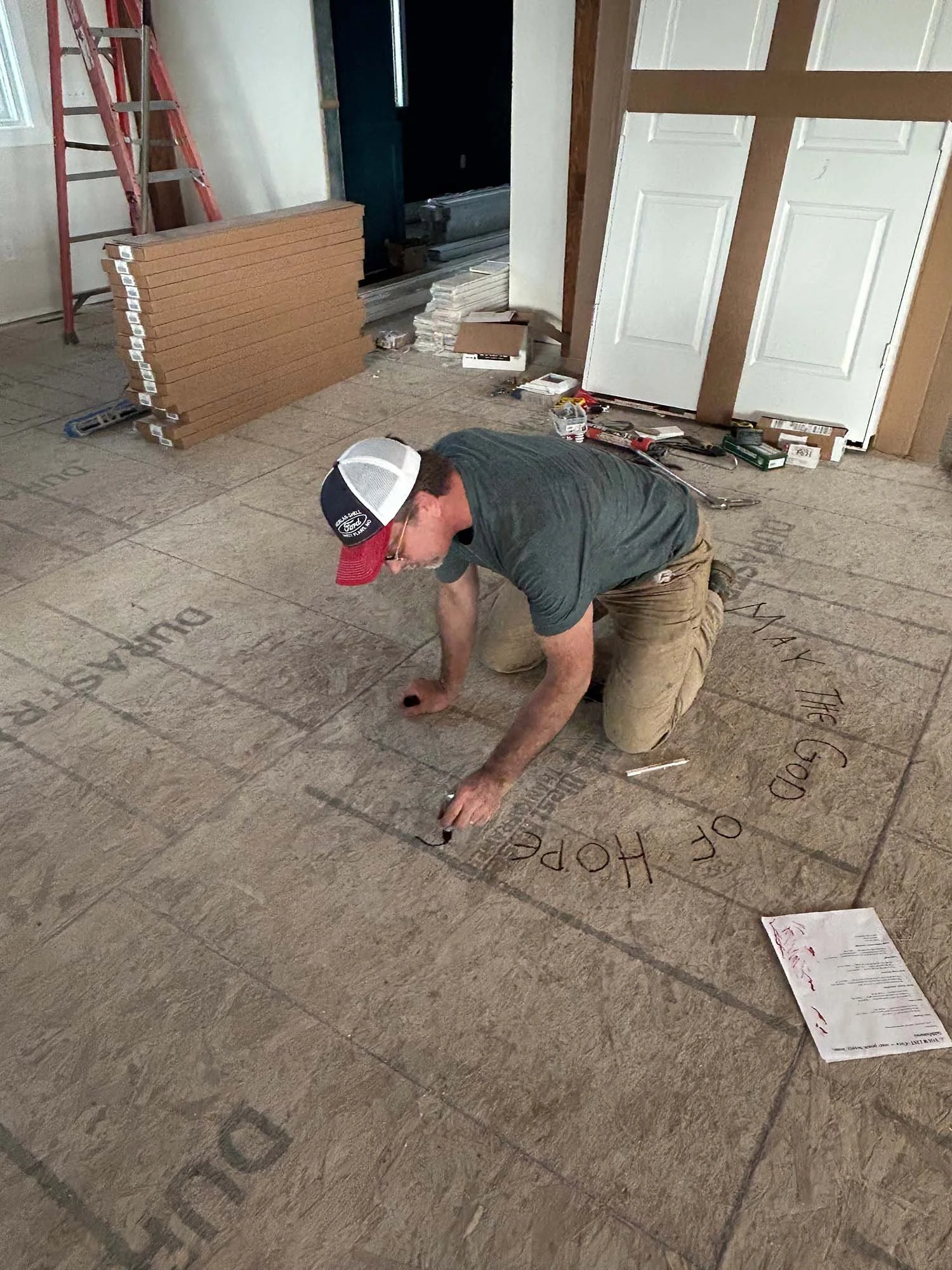 Man writing Bible verses on the unfinished subfloor during construction of our home.
