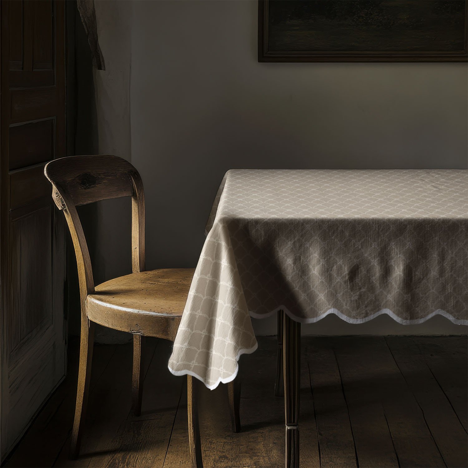 Tan scalloped design on a scalloped edge tablecloth in simple dining room with wood chair and other wood accents.
