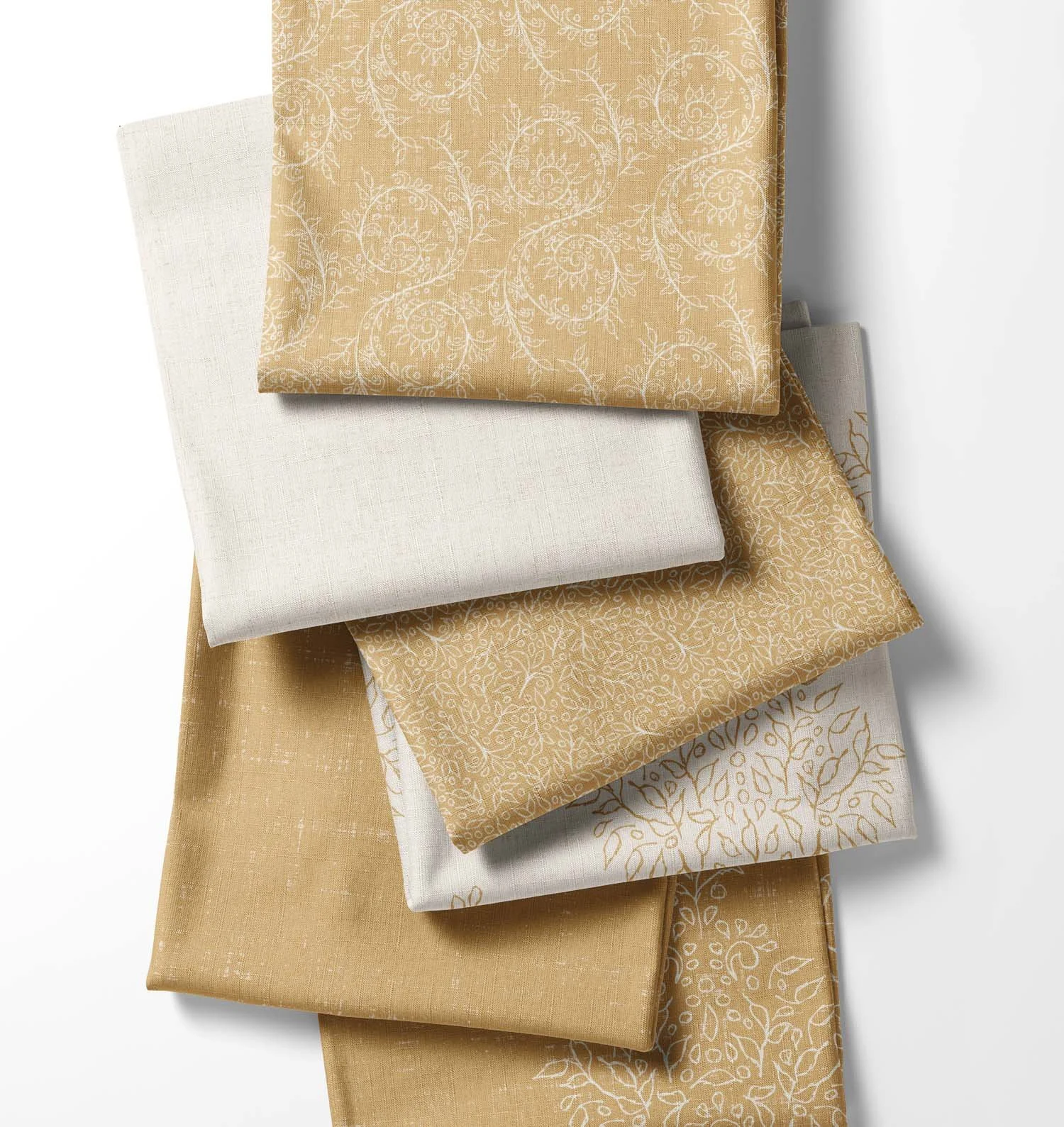 Stack of coordinating gold and antique ivory fabrics from the Grove Vine collection, featuring botanical patterns, damasks and textured linen solids.