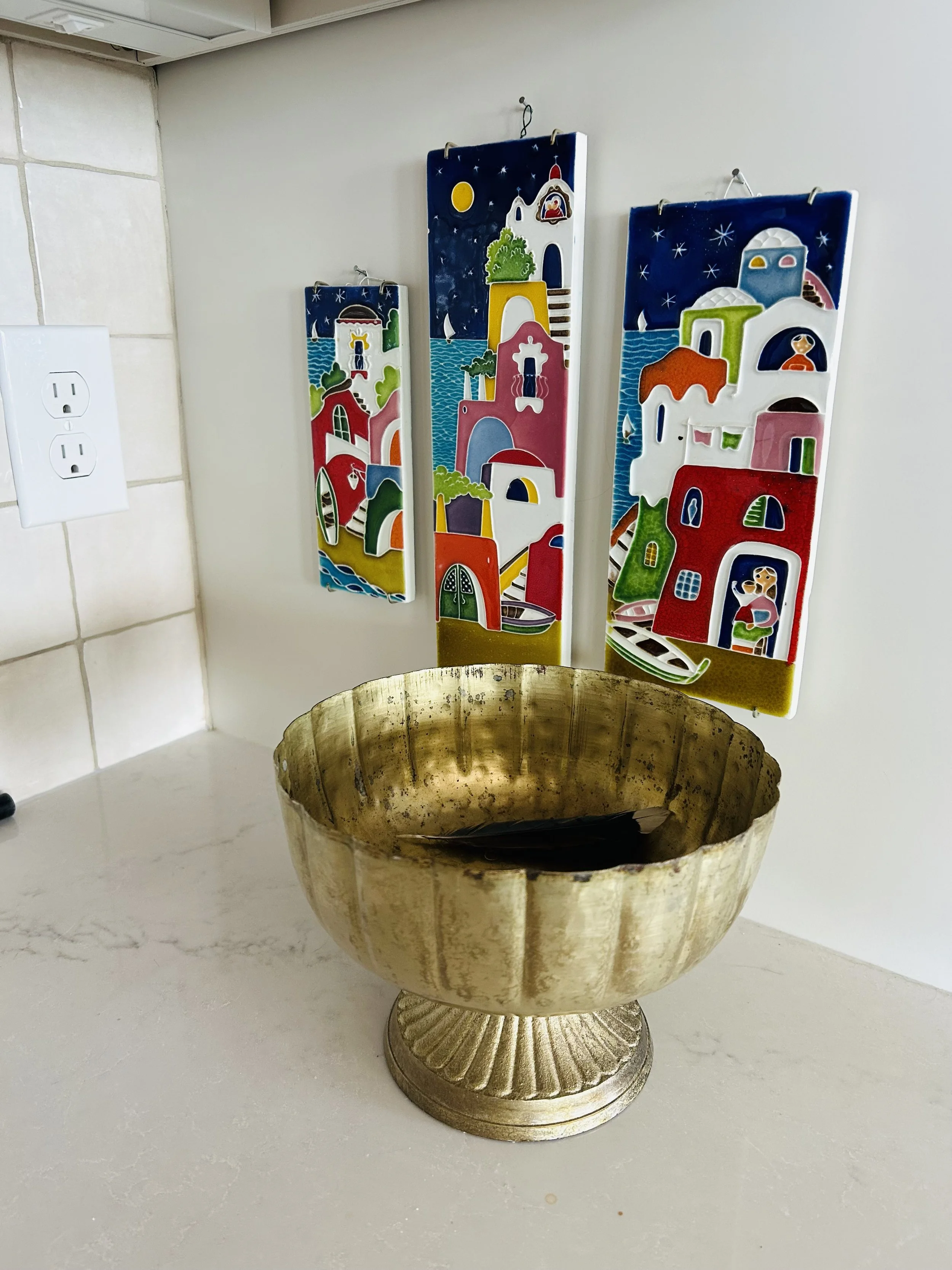Colorful ceramic wall plaques from Cinque Terre displayed above a brass bowl in a farmhouse kitchen.