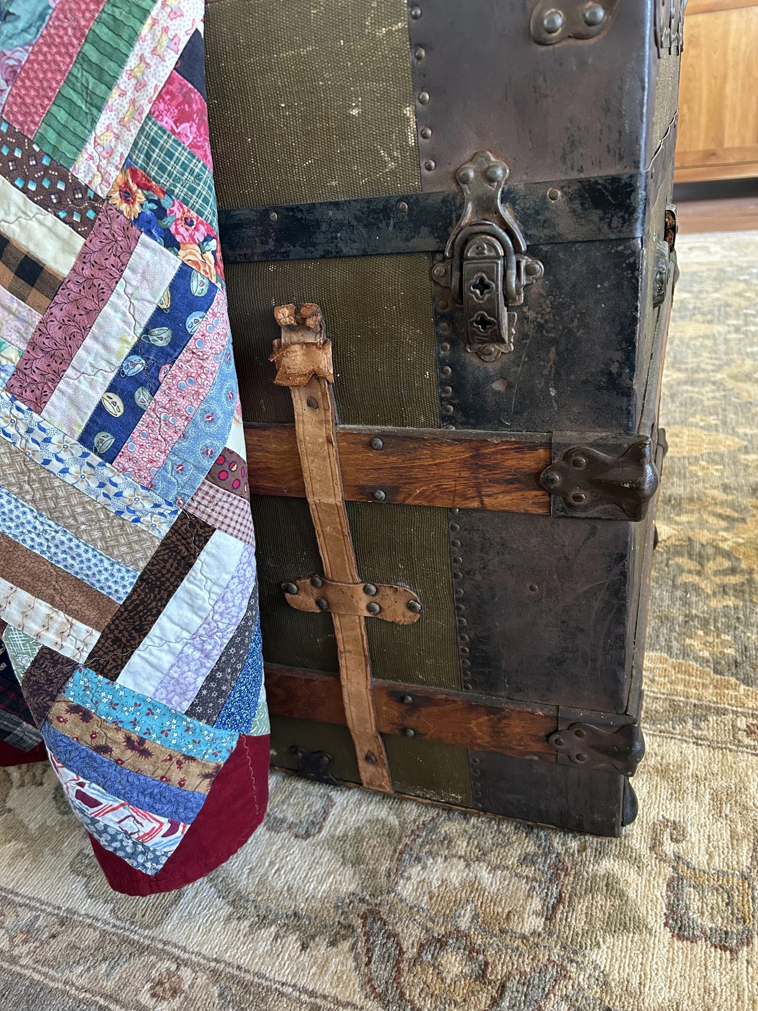 Close view of an antique wood-and-metal trunk beside a colorful handmade family quilt in the Great Room.