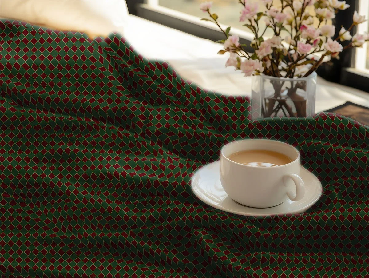 Red and green geometric Christmas fabric draped beside a cup of tea and flowers.