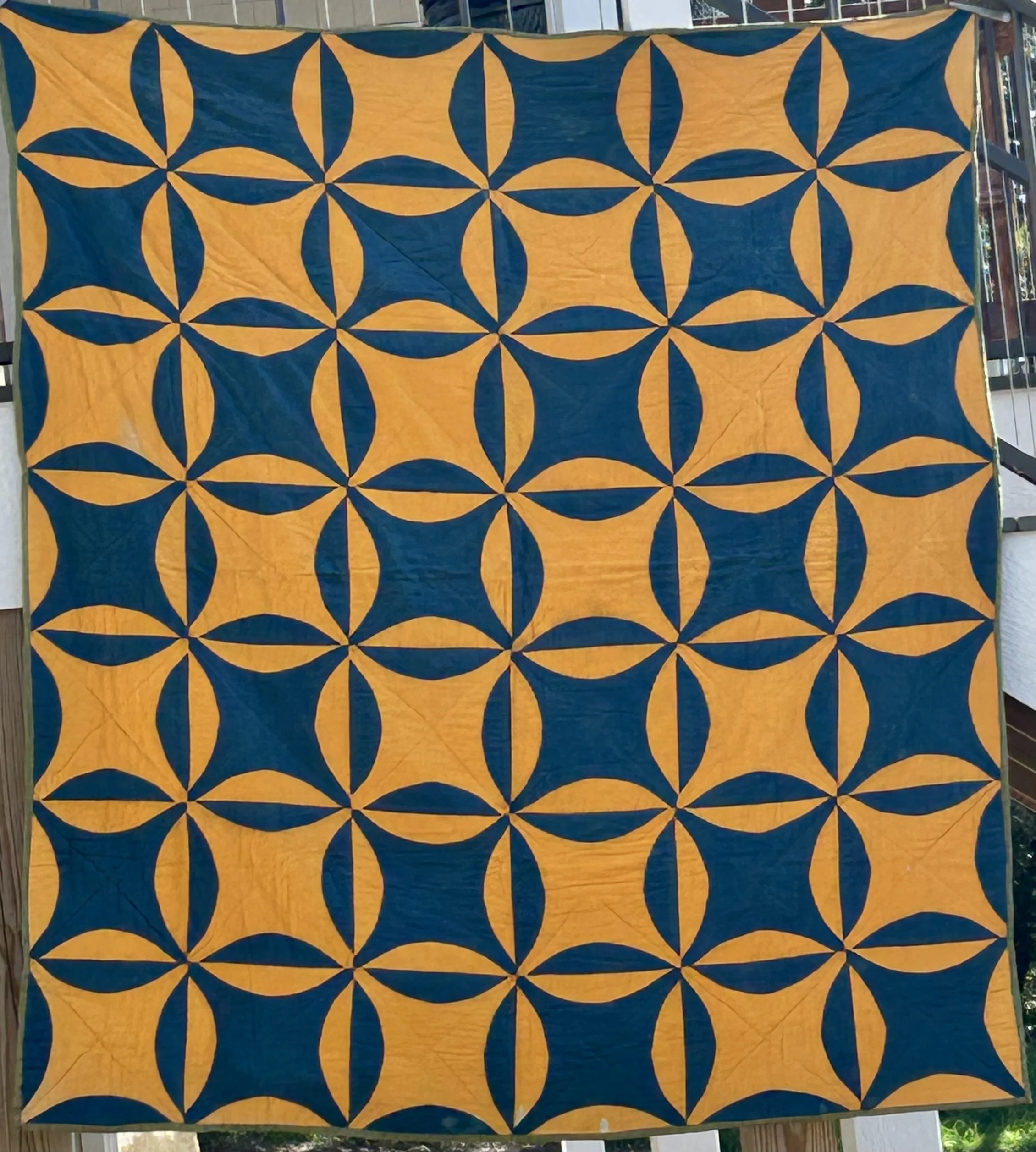Family heirloom quilt with a repeating curved patchwork design in deep teal blue and golden yellow, held up outdoors.