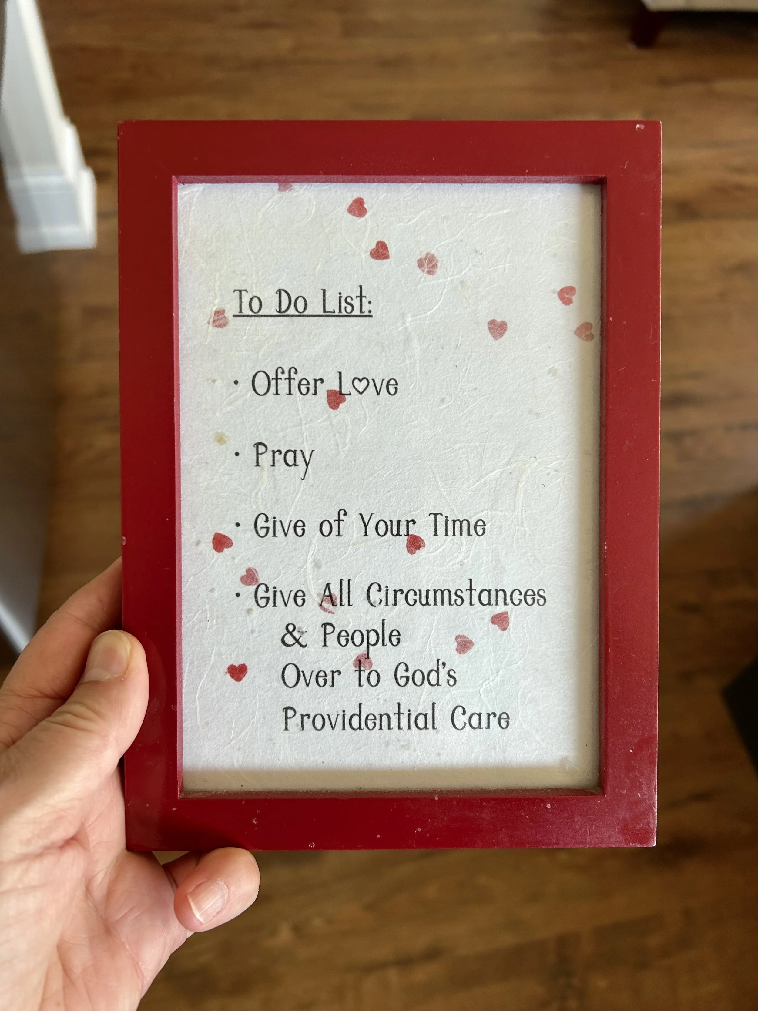 Framed handwritten reminder in a red frame with a daily to-do list: Offer Love, Pray, Give of Your Time, and Give All Circumstances and People Over to God's Providential Care.