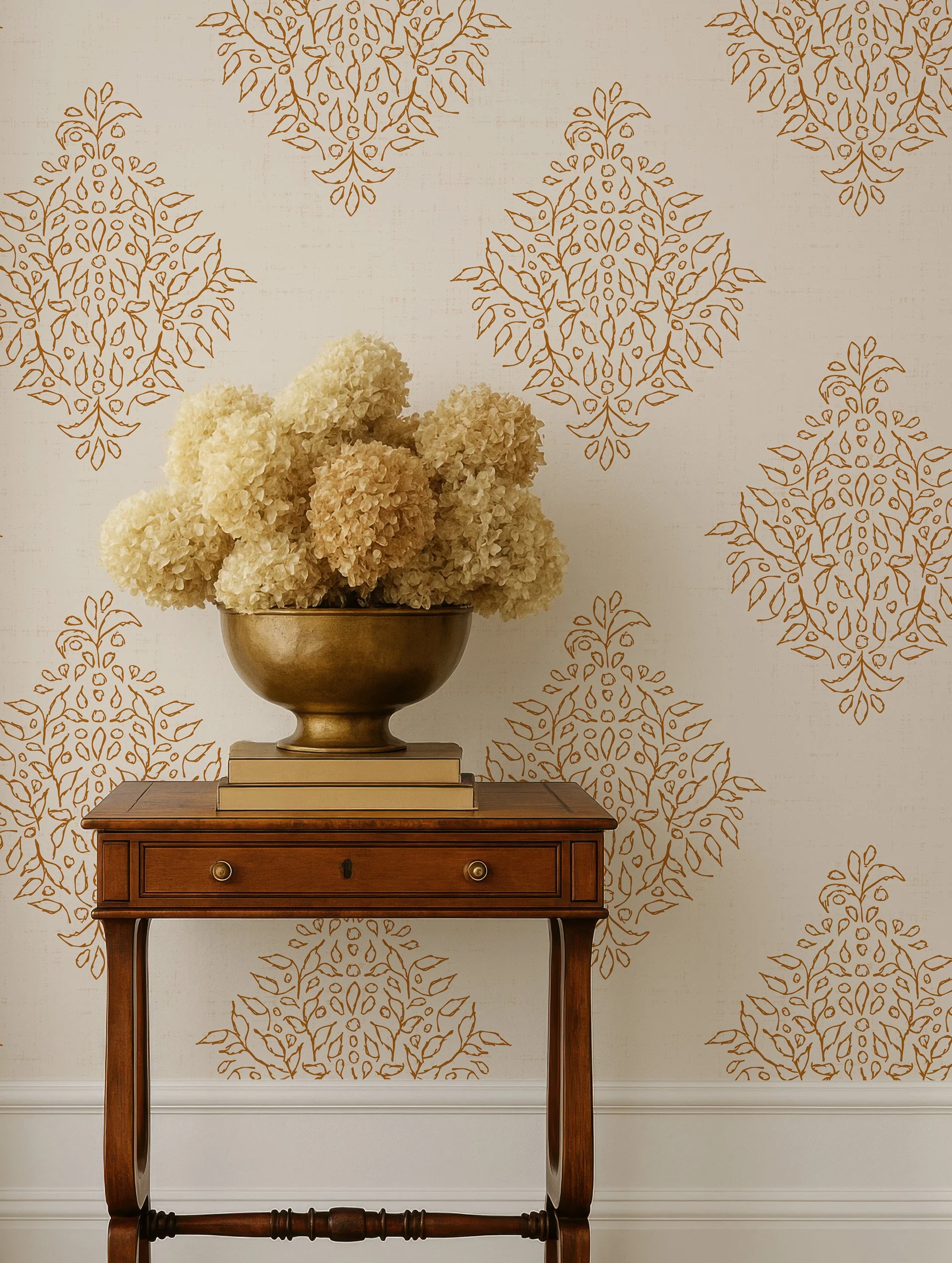 Traditional gold damask wallpaper behind wooden side table with neutral floral arrangement
