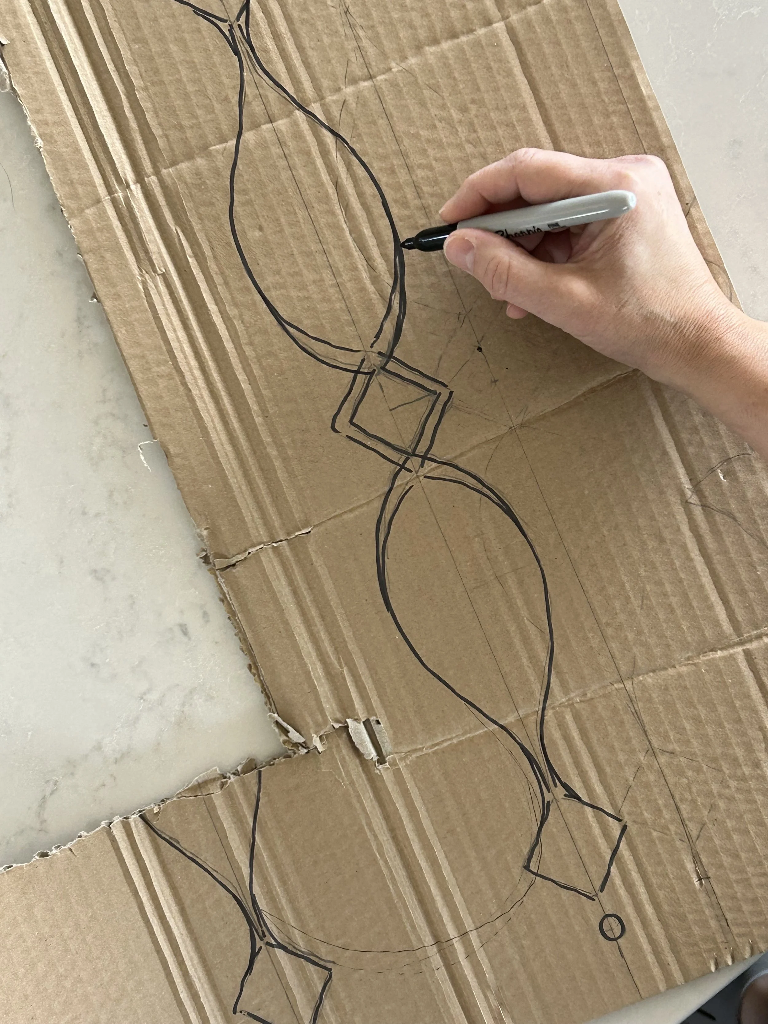 Hand sketching a custom stair railing design on cardboard based on Norwegian architectural inspiration.