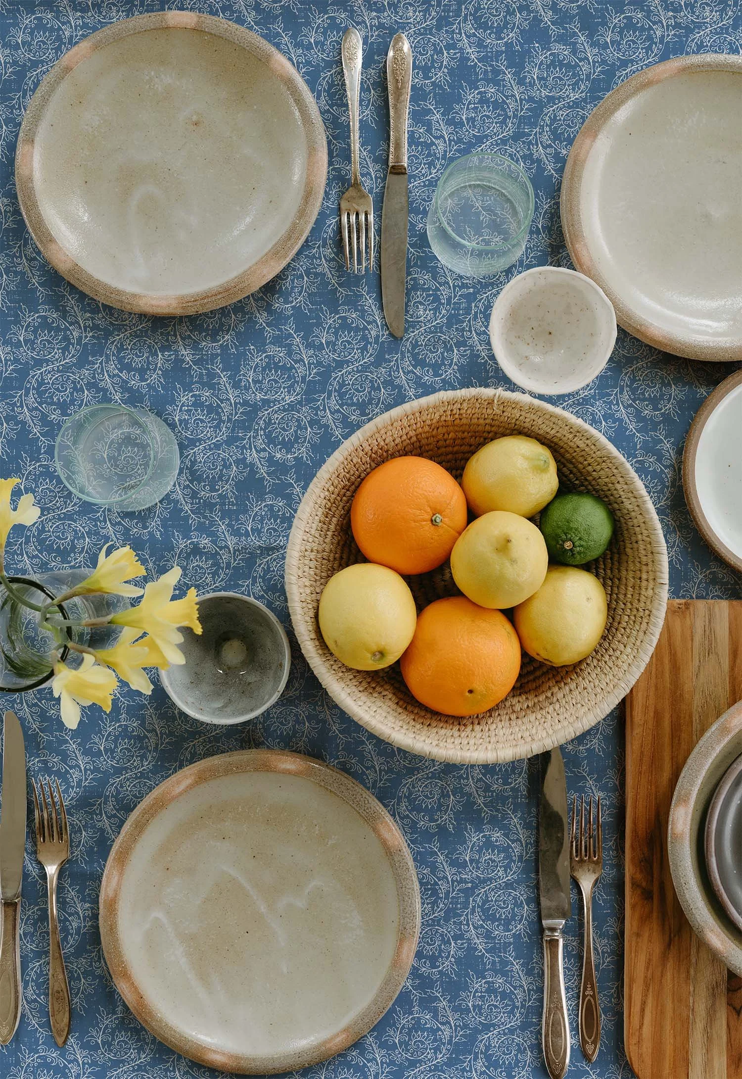 French blue Grove Vine pattern on a summer tablecloth set with handmade ceramic dishes, fresh citrus fruit and yellow flowers.