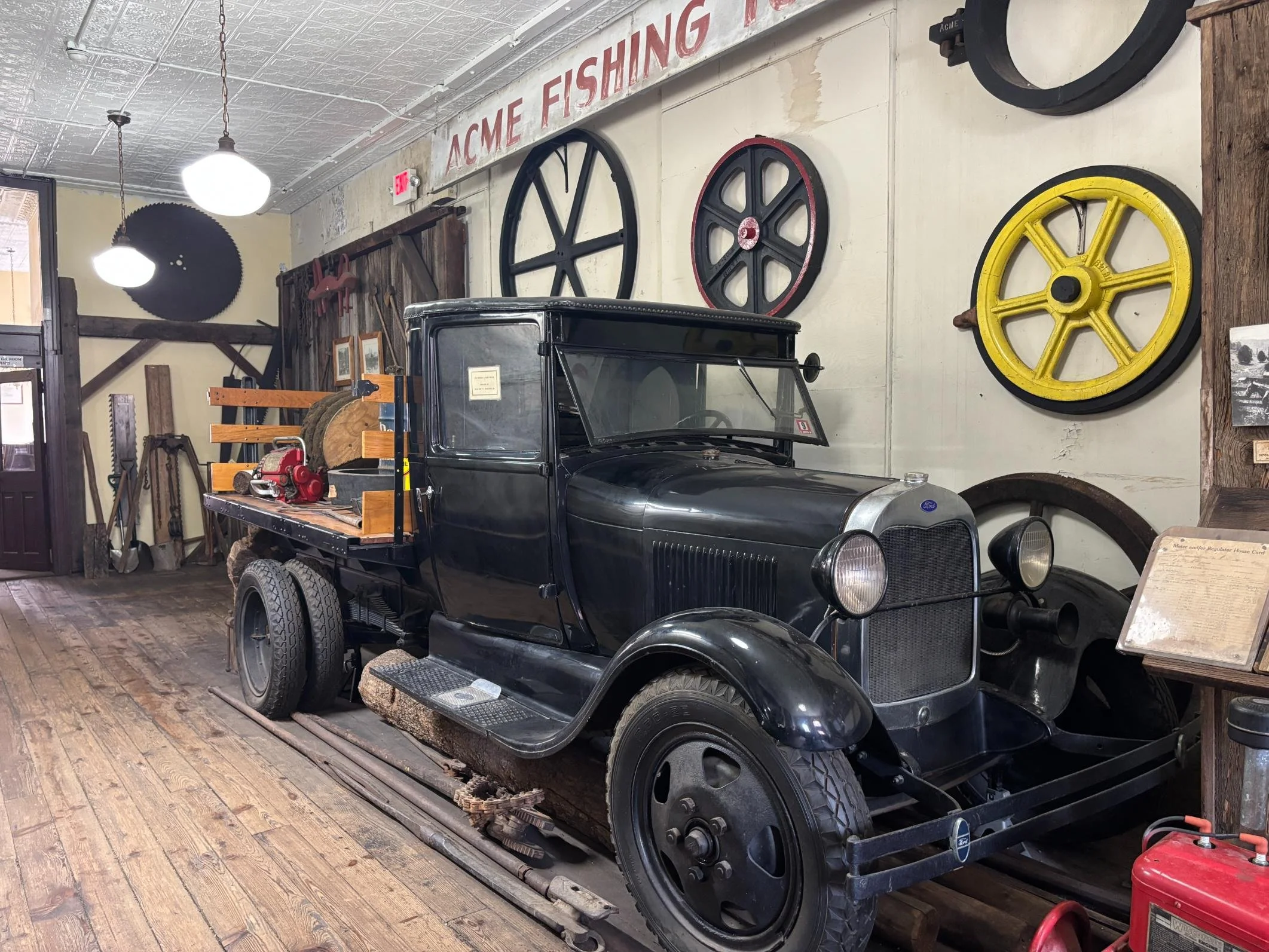 Vintage black Ford pickup truck displayed inside a museum with large wooden wheels hanging on the wall behind it.