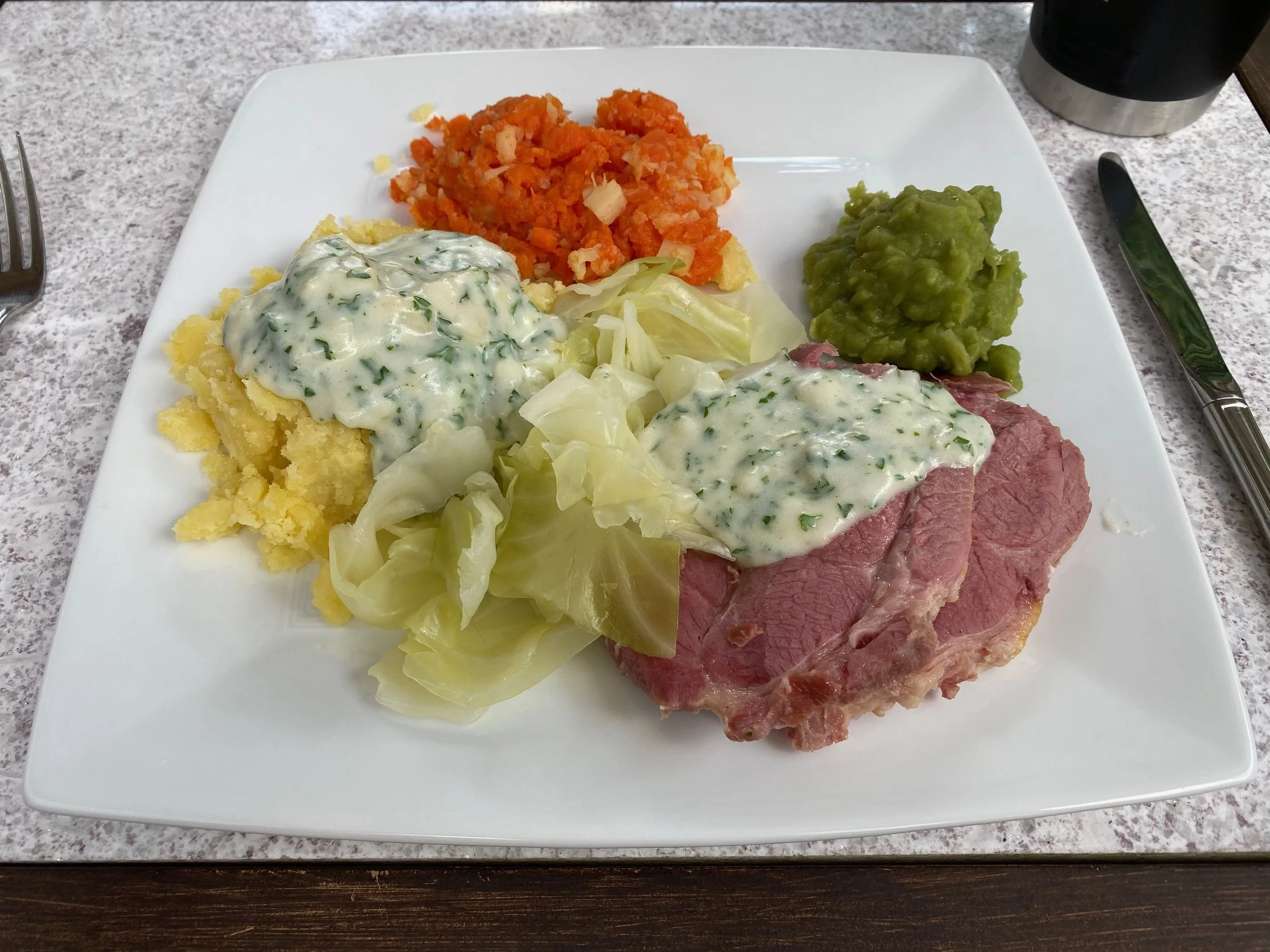 a square white plate with Irish bacon and cabbage, potatoes, carrots, peas