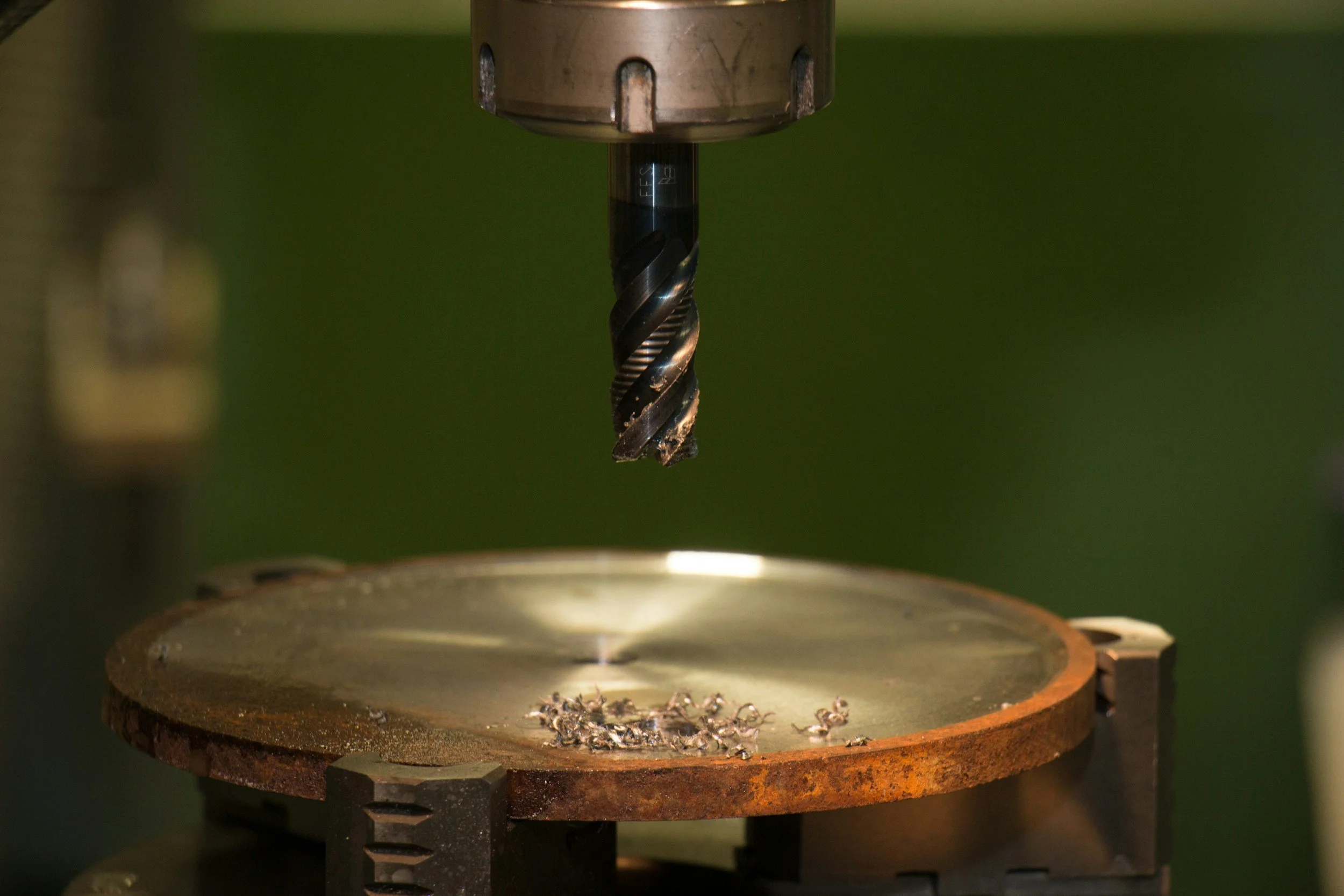 A CNC machine drill bit positioned above a round metal workpiece with small metal shavings on its surface.