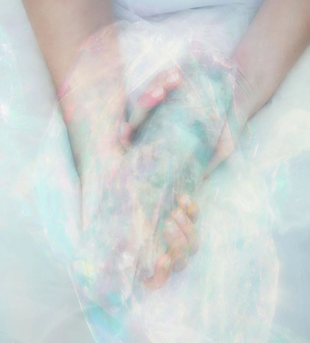 A close-up of two hands gently holding a clear crystal wand against a light, iridescent background.