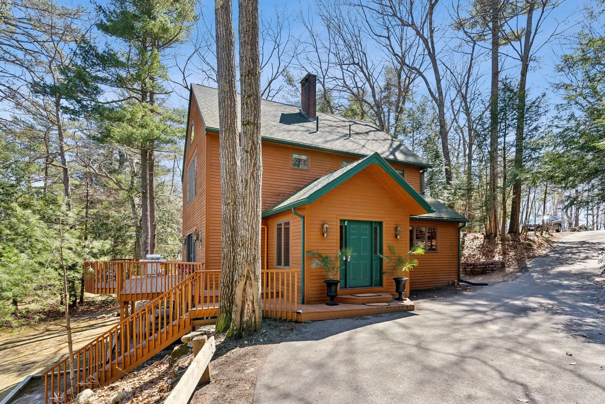 Wooden cabin surrounded by trees with a green door and deck.