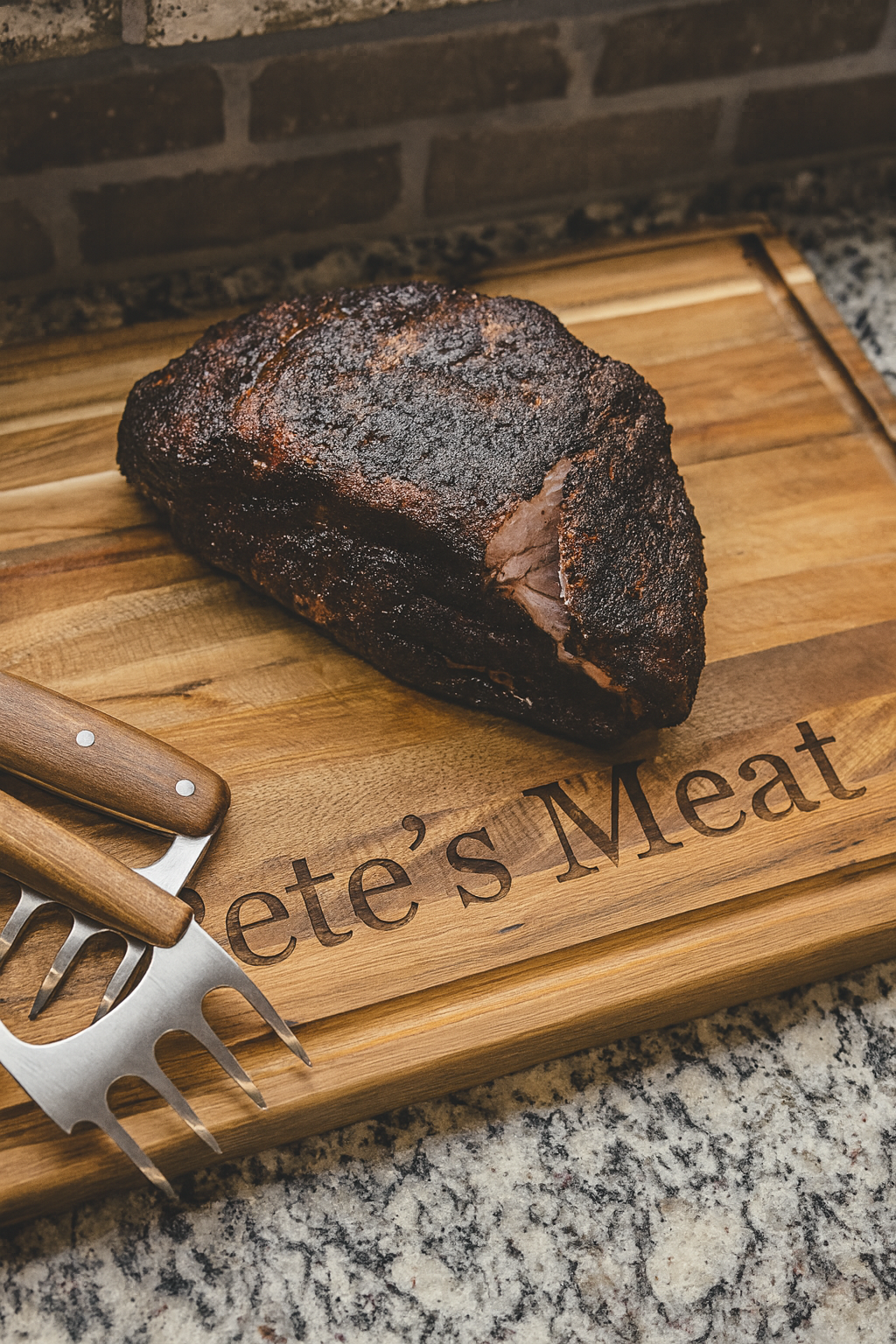 A smoked beef brisket with a dark, crispy bark resting on a wooden cutting board labeled "Pete's Meat." There is a meat fork and a carving knife with a wooden handle alongside the brisket.