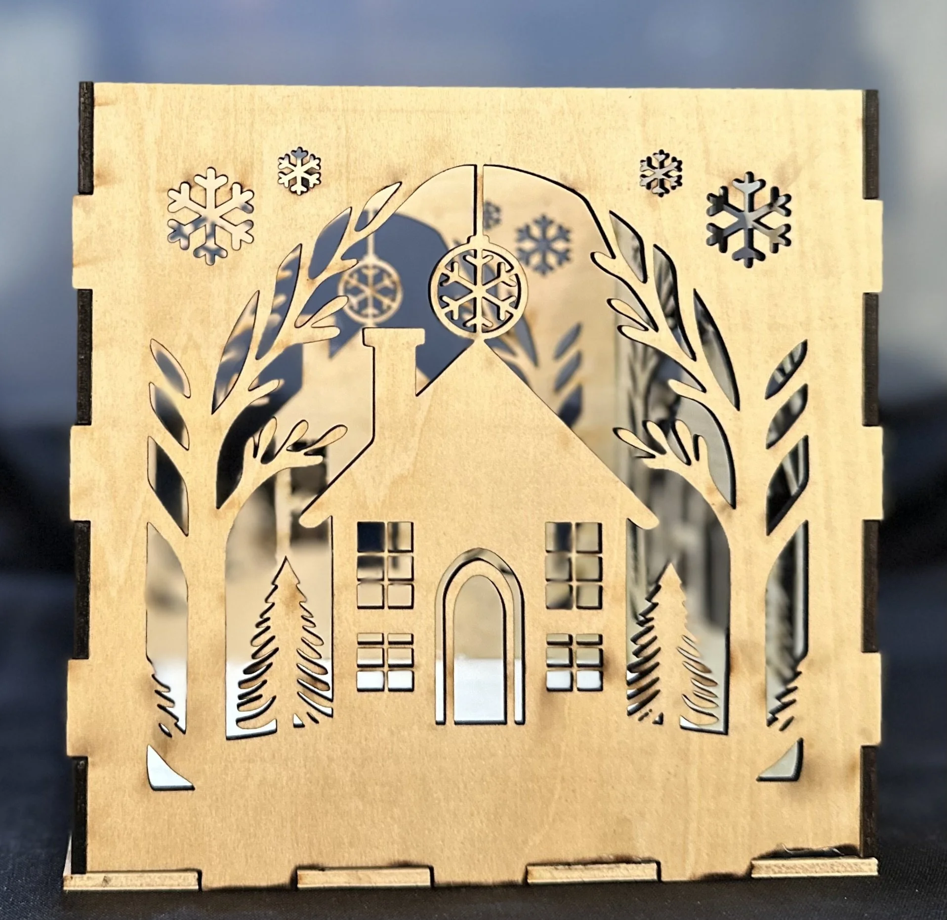 Wooden decorative box with laser-cut house, trees, snowflakes, and ornaments design.