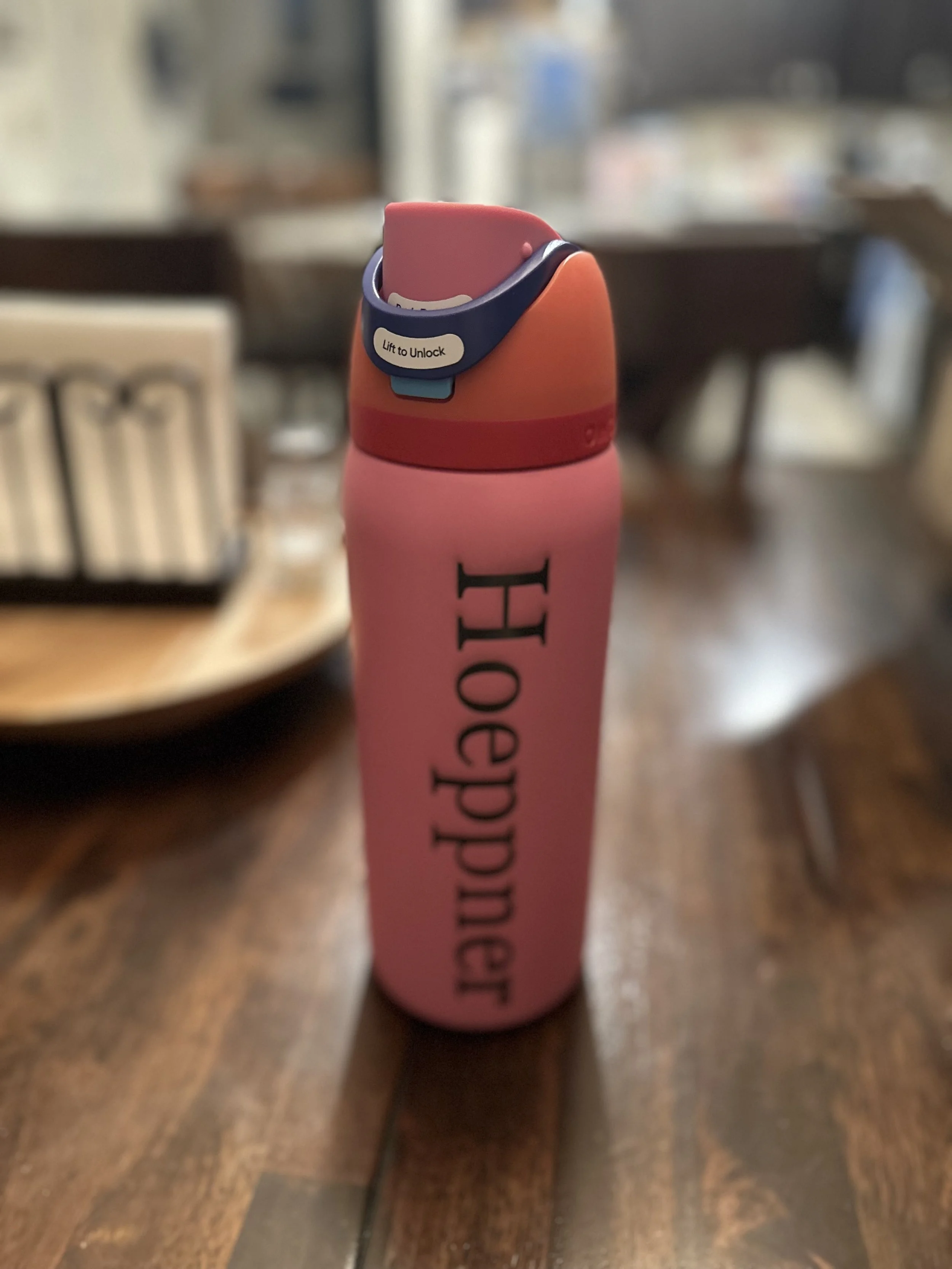 Pink personalized water bottle on a wooden table.