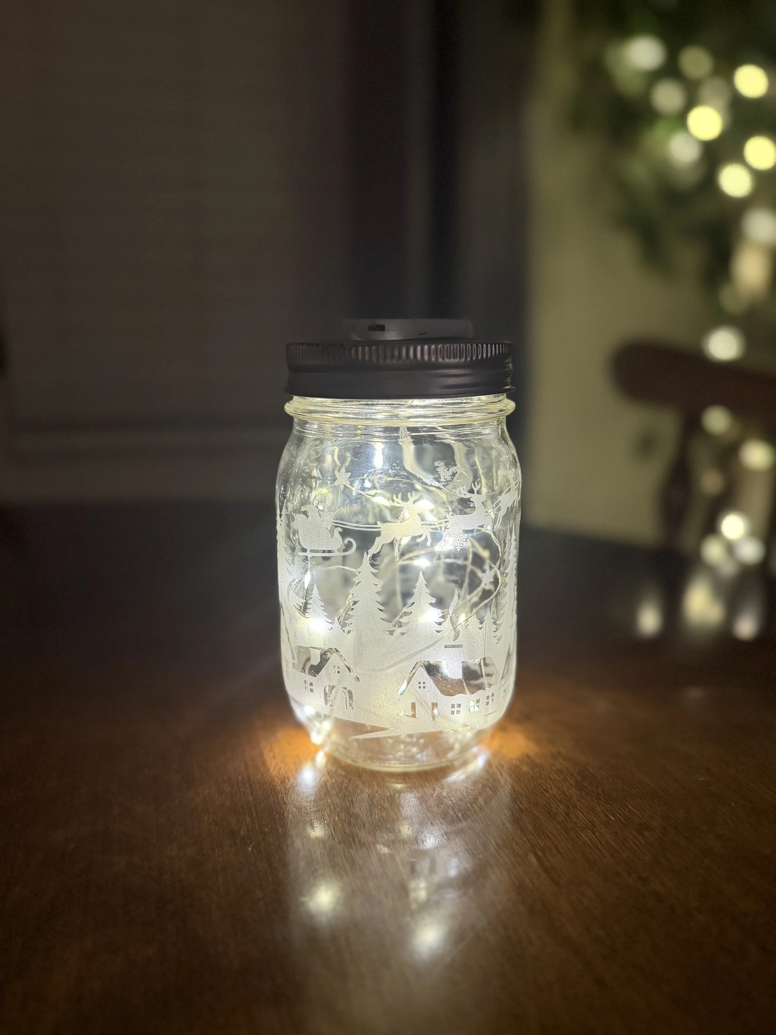 This is a great example of glass etching, which we do on a number of products including pint glasses, mirrors, decanters, and wine glasses. The Ball canning jar was wrapped with a Christmas scene, and then lit with a strand of battery operated fairy 