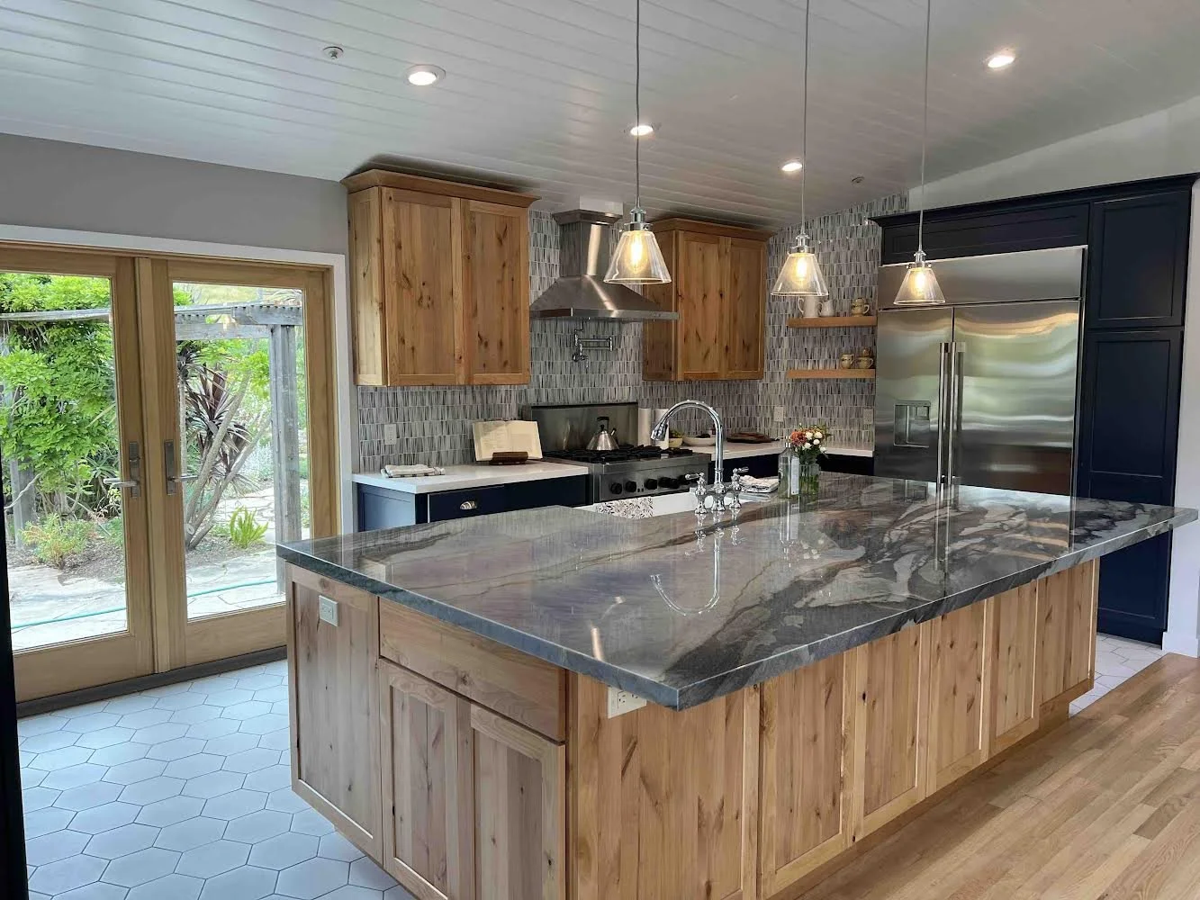 Modern kitchen with wooden cabinets, granite island, stainless steel appliances, and sliding glass door to outside garden.