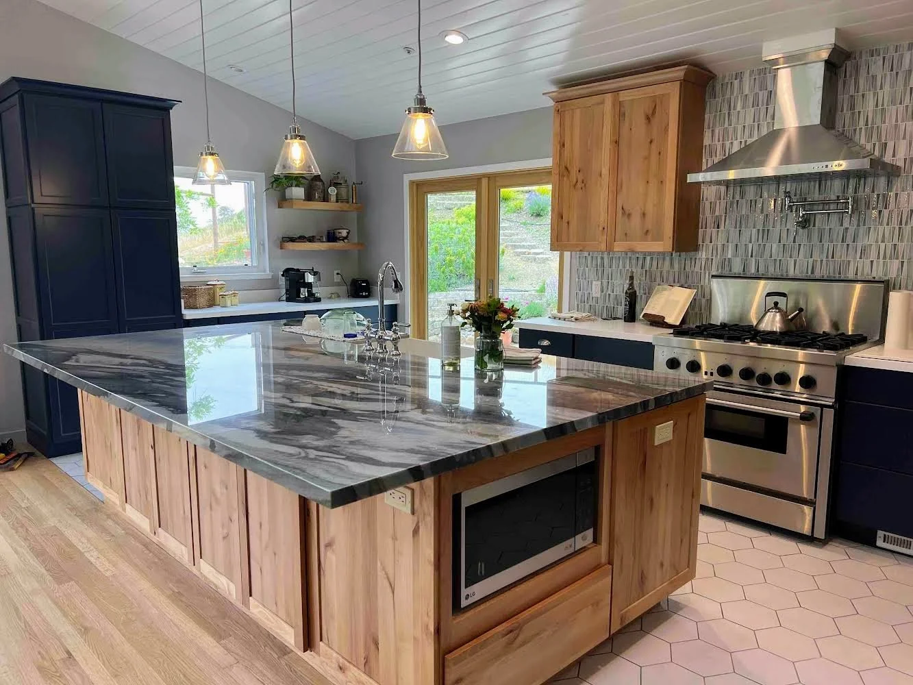 Modern kitchen with a large marble island, wooden cabinetry, stainless steel stove and range hood, hexagonal floor tiles, and pendant lighting.