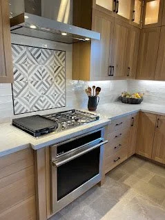 Modern kitchen with wooden cabinets, a stove, a textured tile backsplash, and a black utensil holder with cooking tools.