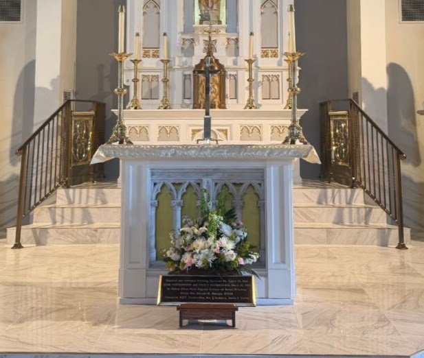 Interior of a church altar with floral arrangements, candles, and religious decor.