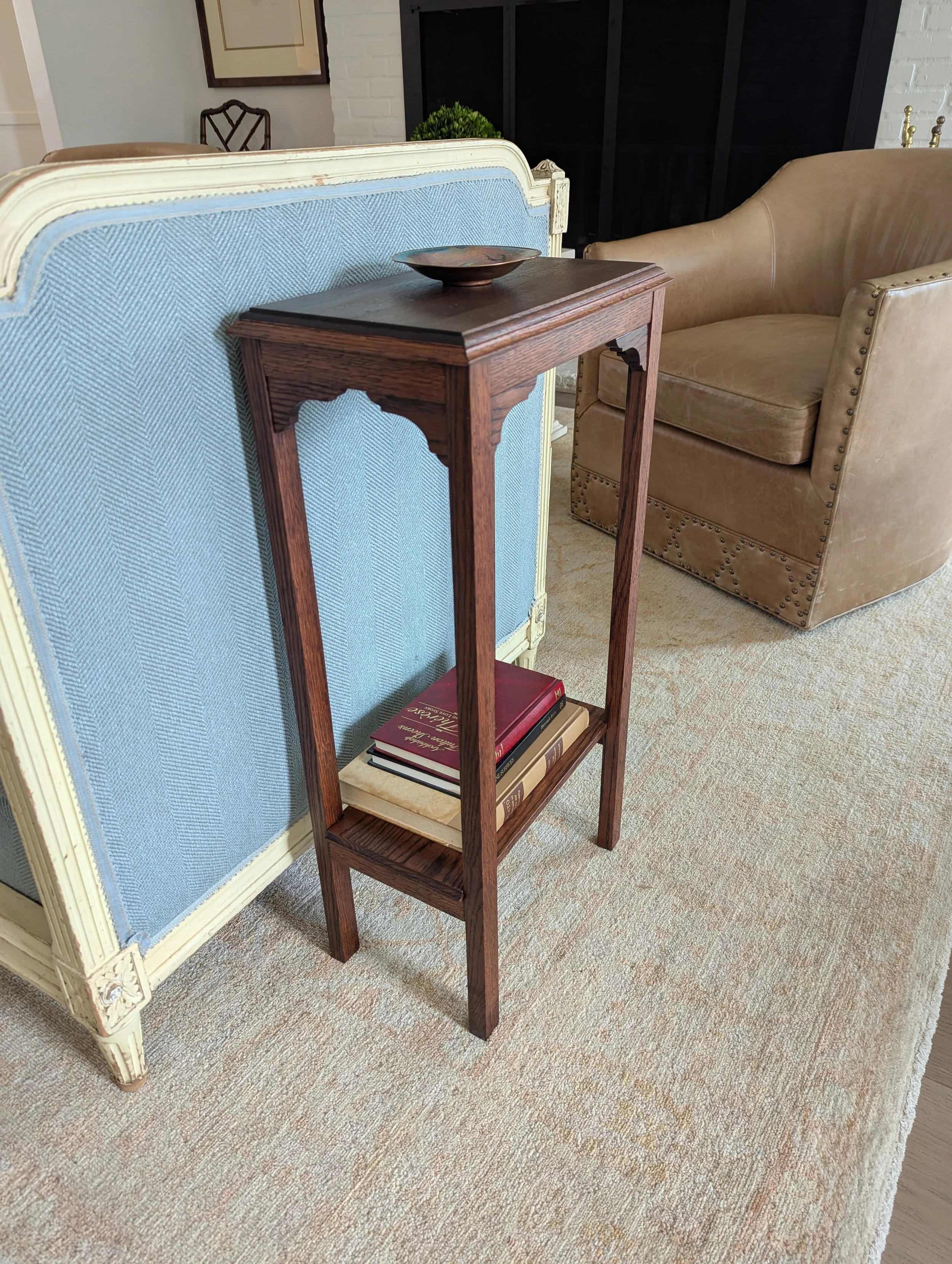A small wooden table with books and a decorative bowl on top, next to a vintage light blue upholstered sofa in a cozy living room with a beige armchair and framed pictures on the wall.
