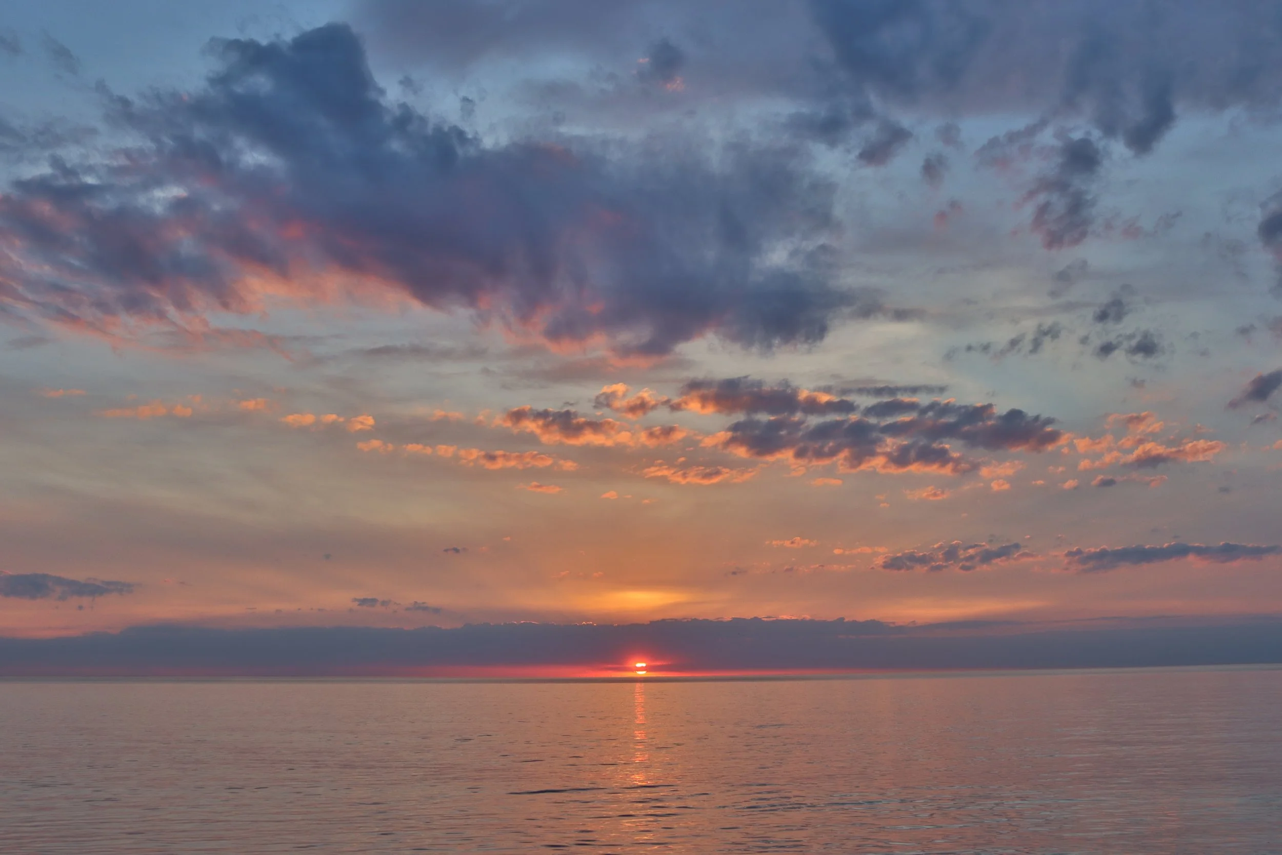 Ein Sonnenuntergang über dem ruhigen Meer mit bunten Wolken am Himmel.
