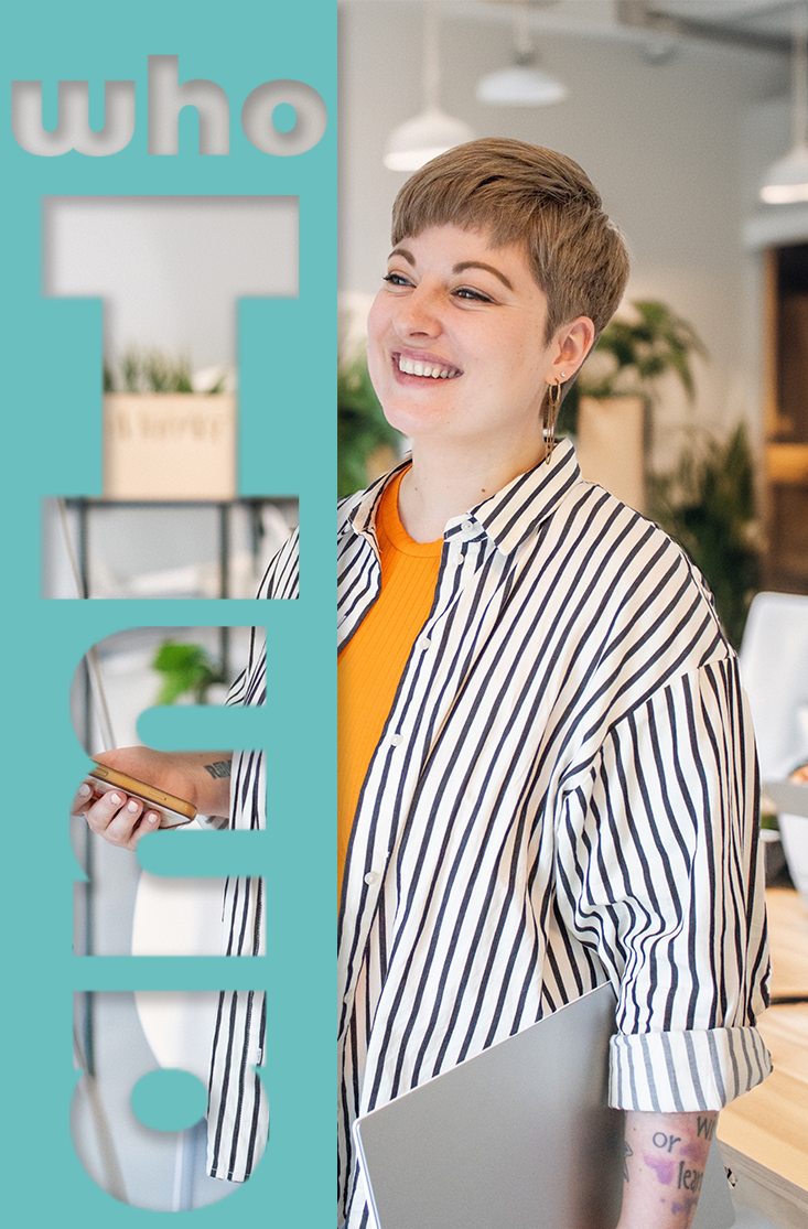 Eine lachende Frau mit Kurzhaarfrisur und gestreiftem Hemd hält ein Smartphone in der Hand in einem modernen Büro.