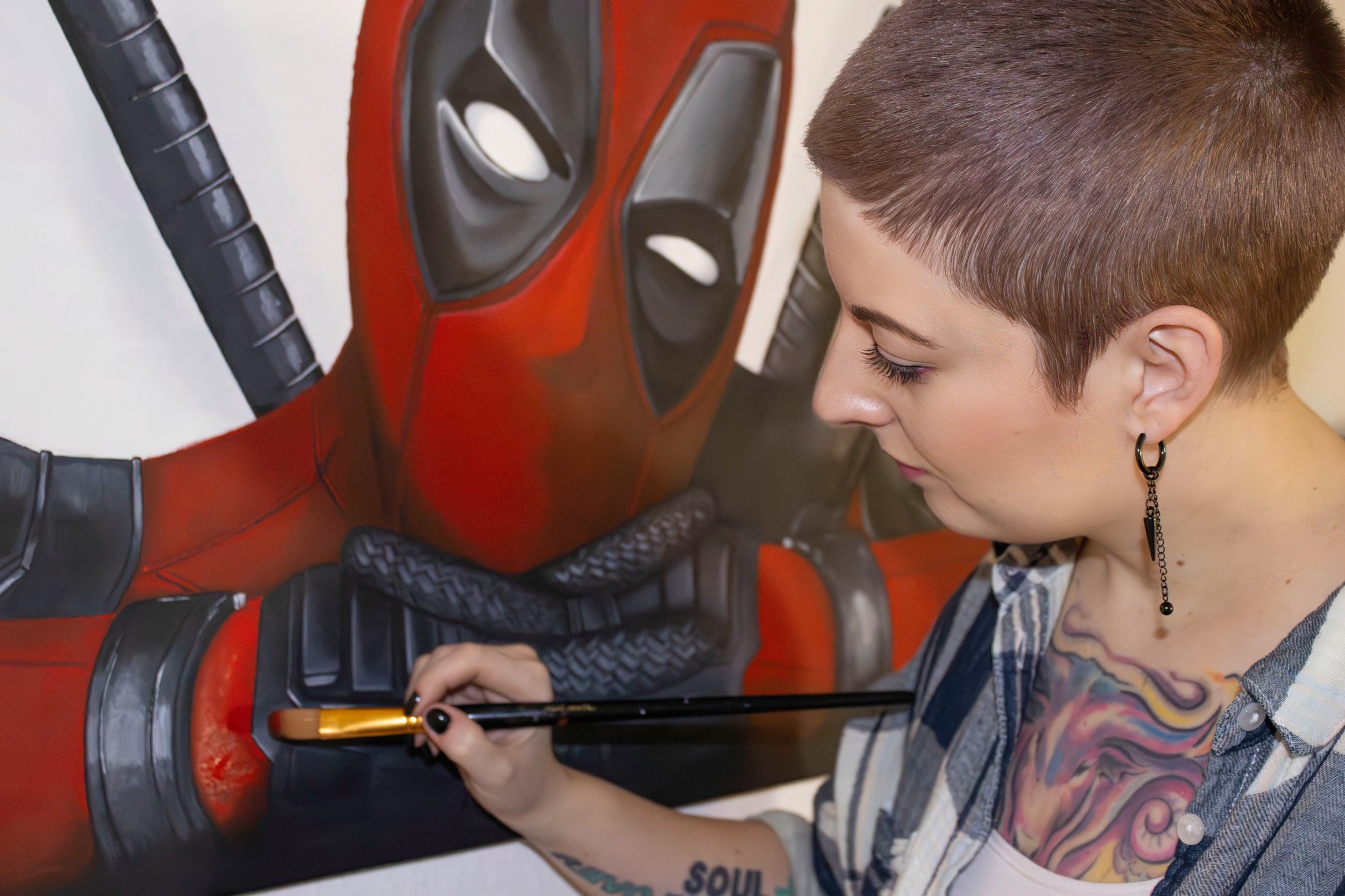 Künstlerin malt ein Wandbild von Deadpool auf eine weiße Wand.