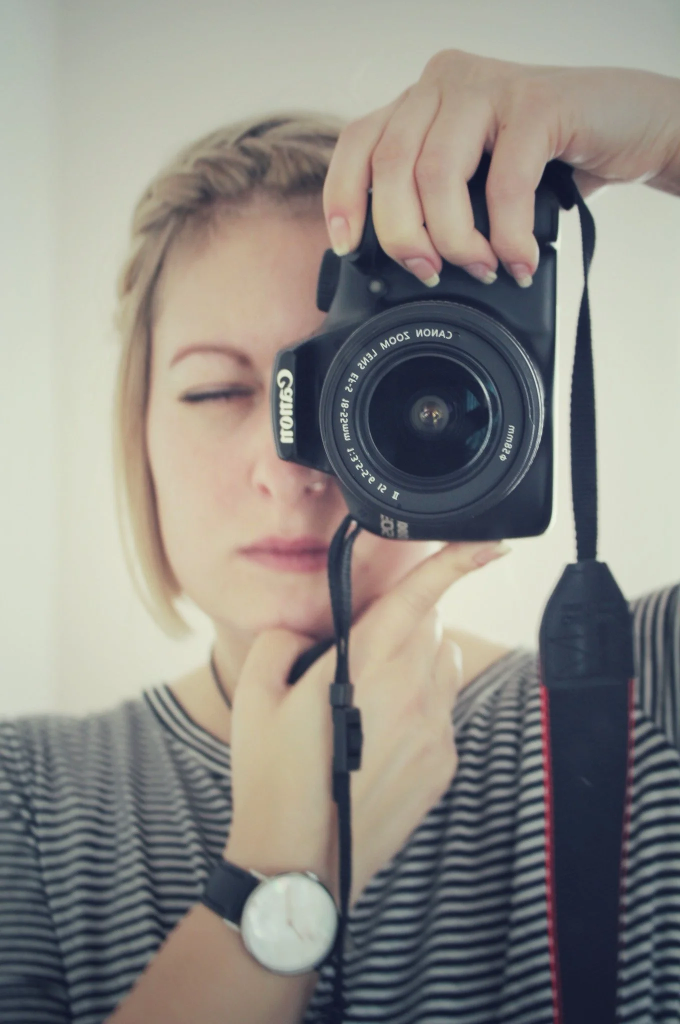 Eine Frau, die eine Kamera vor ihrem Gesicht hält und ein Selbstporträt macht, trägt ein gestreiftes Oberteil und eine Armbanduhr.