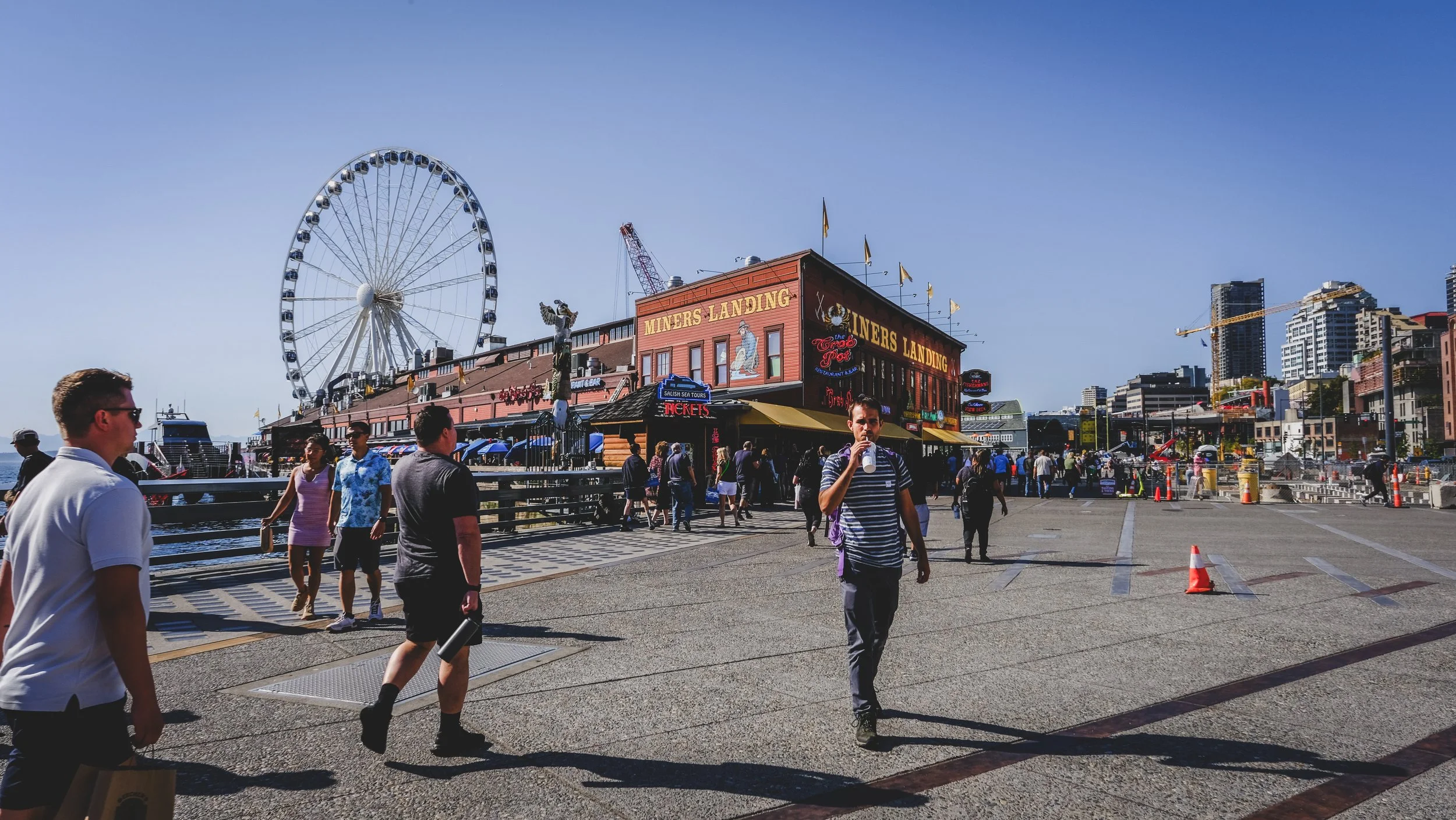 People walking along a pier with a large Ferris wheel and a building labeled 'Miners Landing' in Seattle, Washington.
