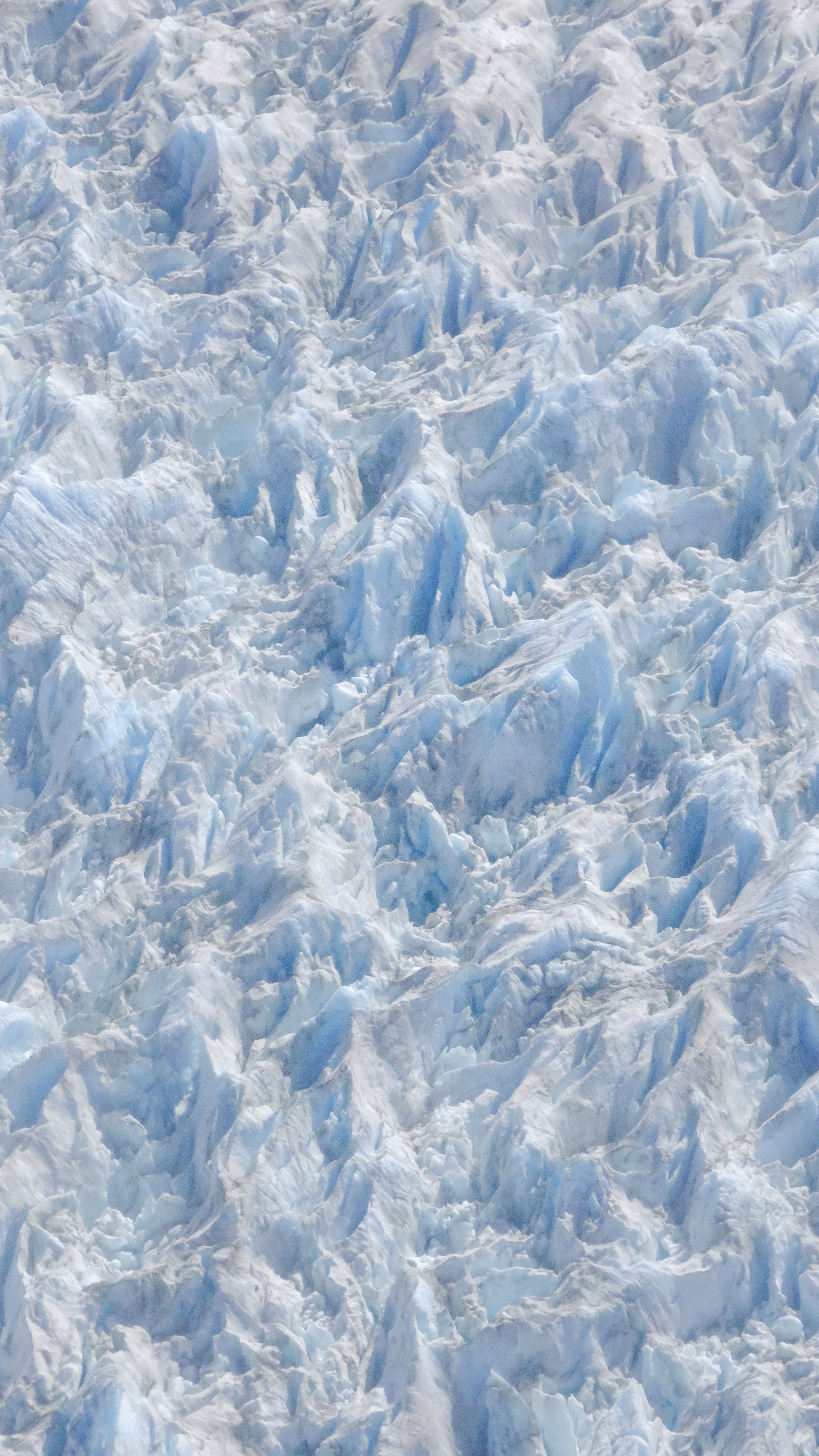 Aerial view of a vast expanse of rugged, icy glaciers with sharp, jagged peaks and deep crevices.