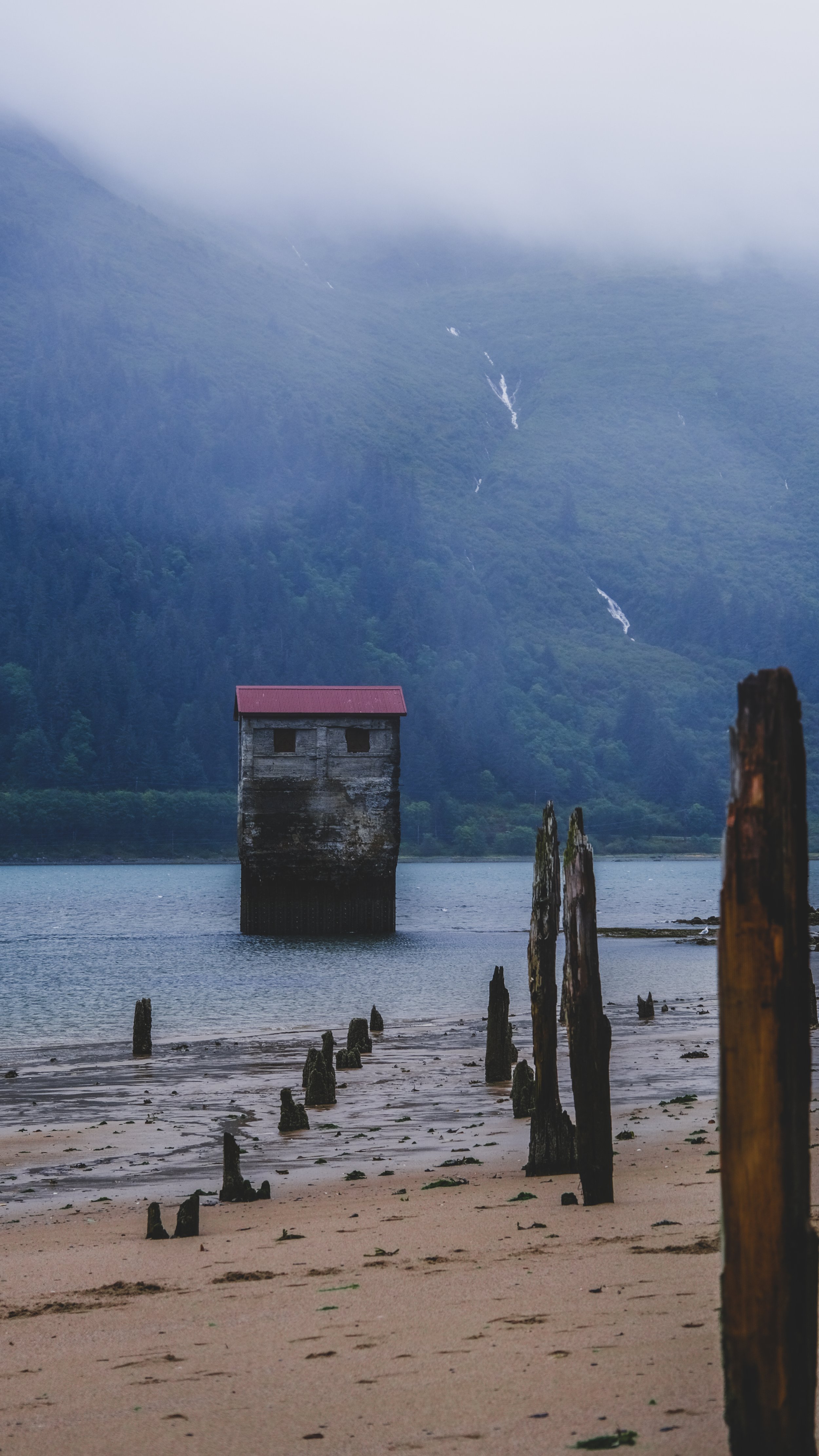A wooden structure on stilts in a calm lake with a mountain in the background, partially obscured by fog.