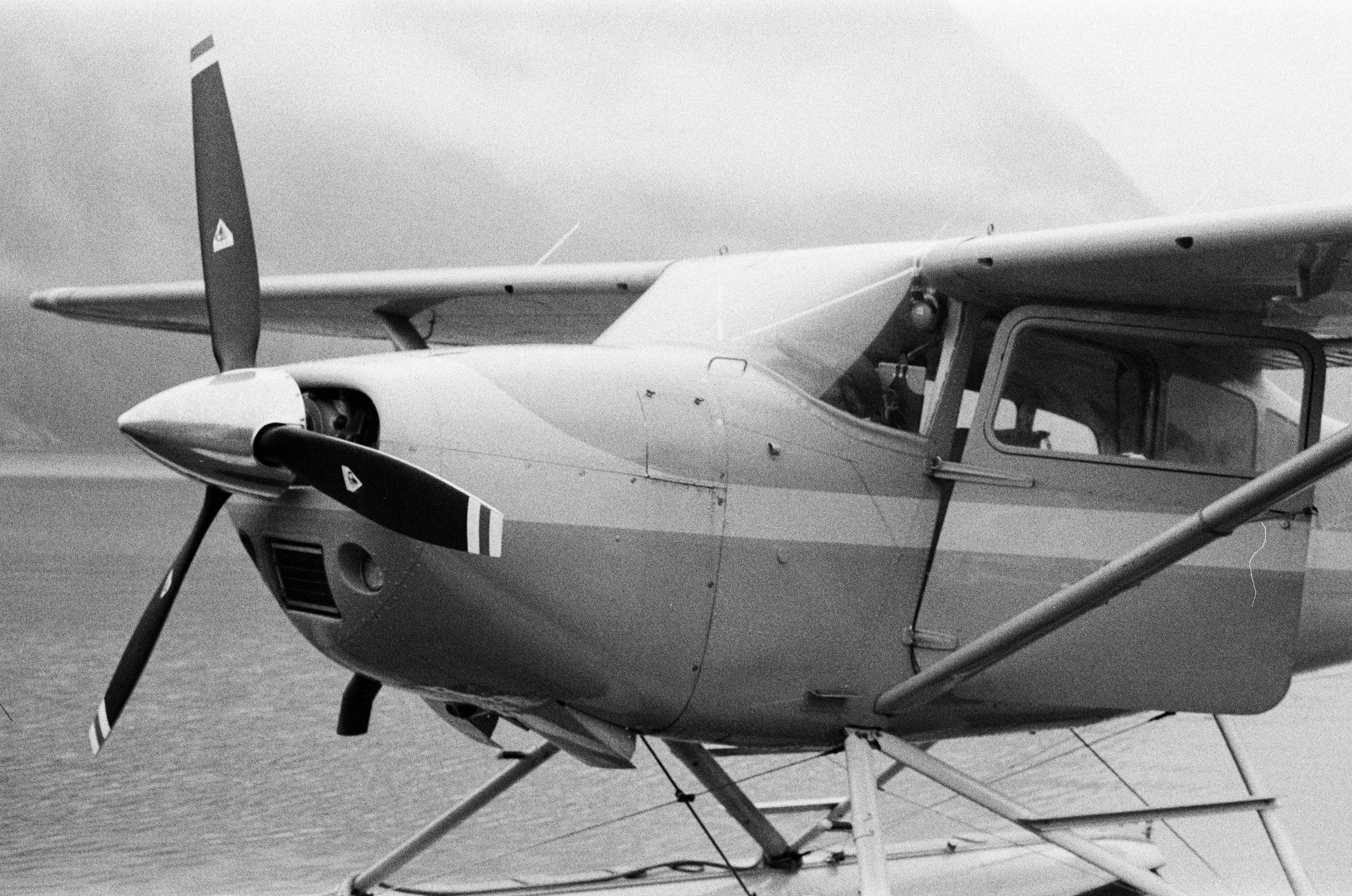Black and white photo of a small seaplane on water, with its propeller and cockpit visible.