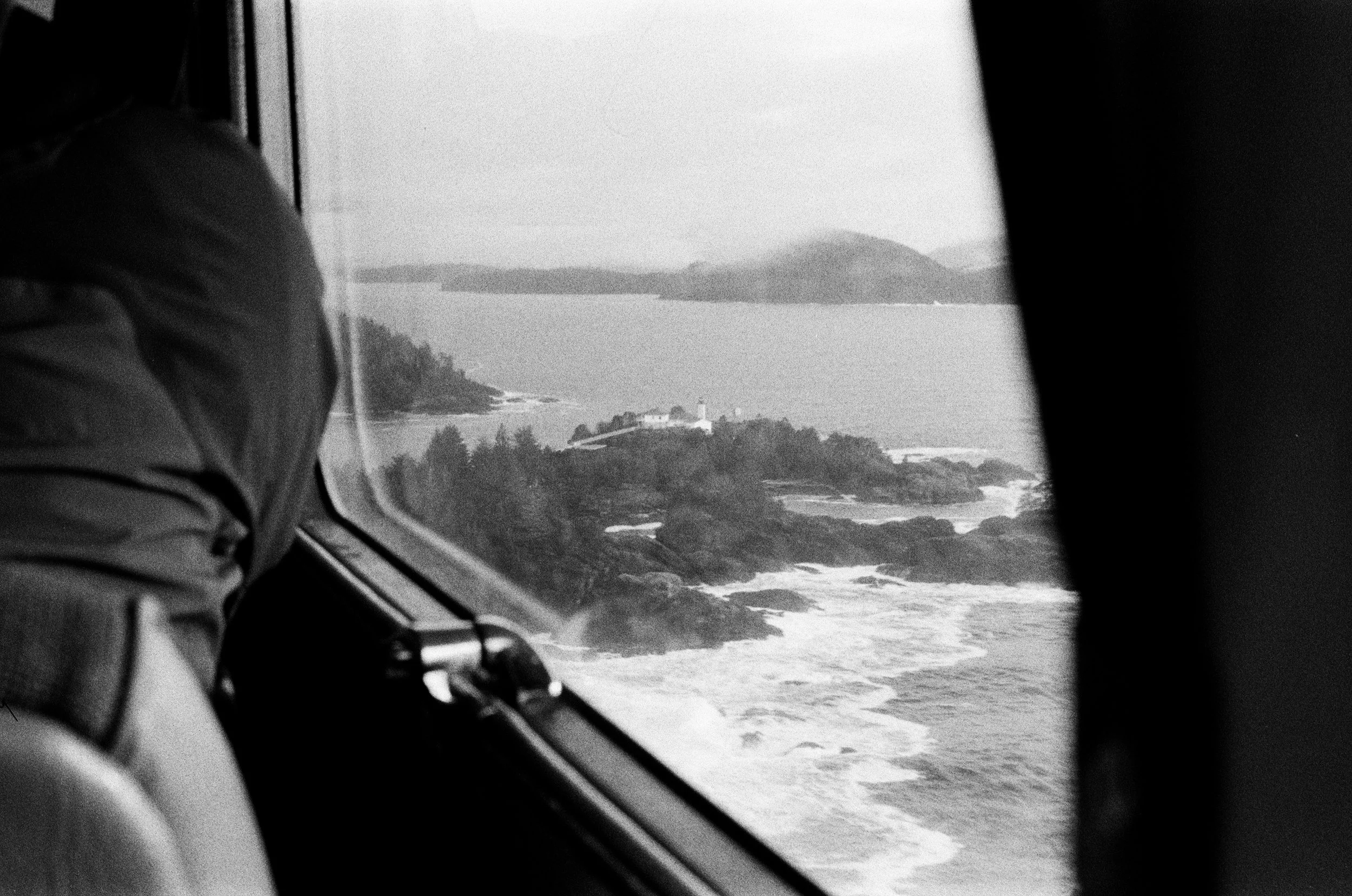 View of the ocean and rocky coastline through an aircraft window.