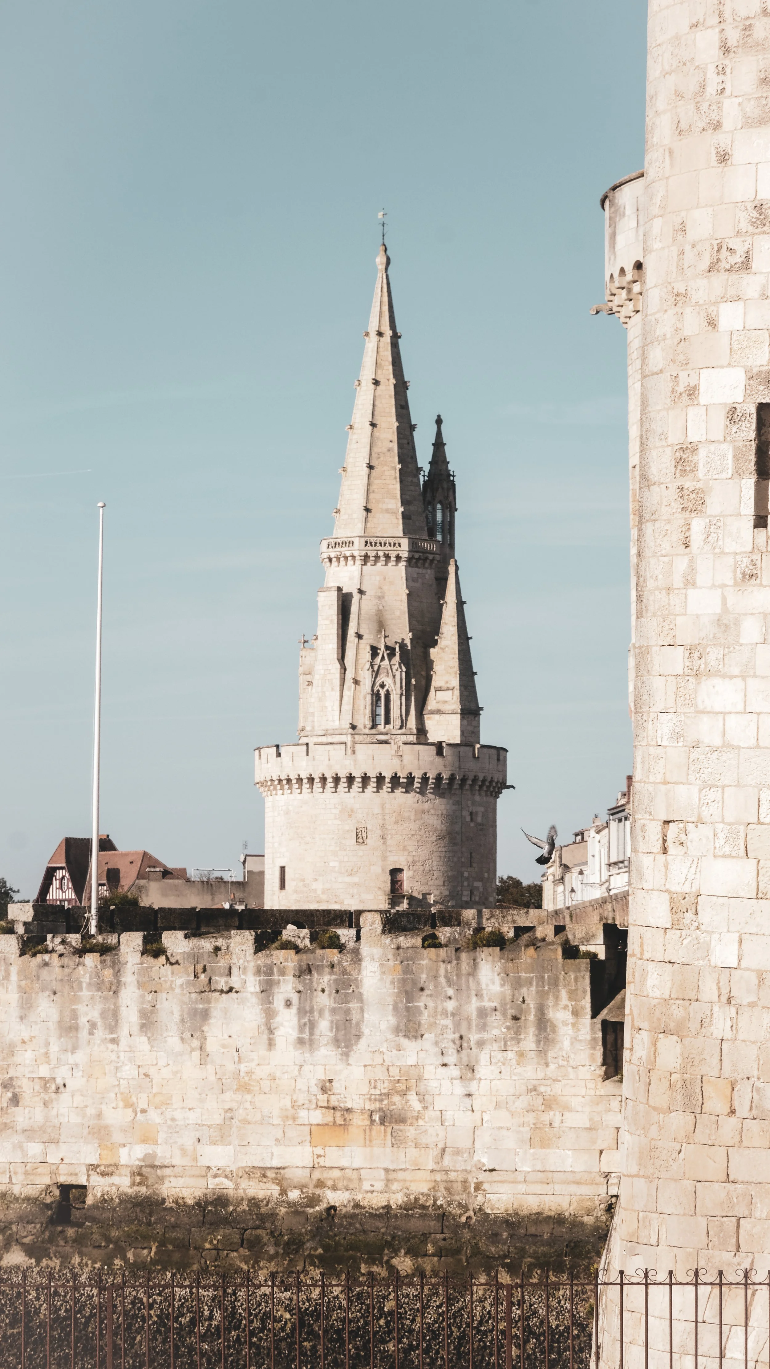 A historic stone tower with a pointed spire, part of a castle, against a clear blue sky.