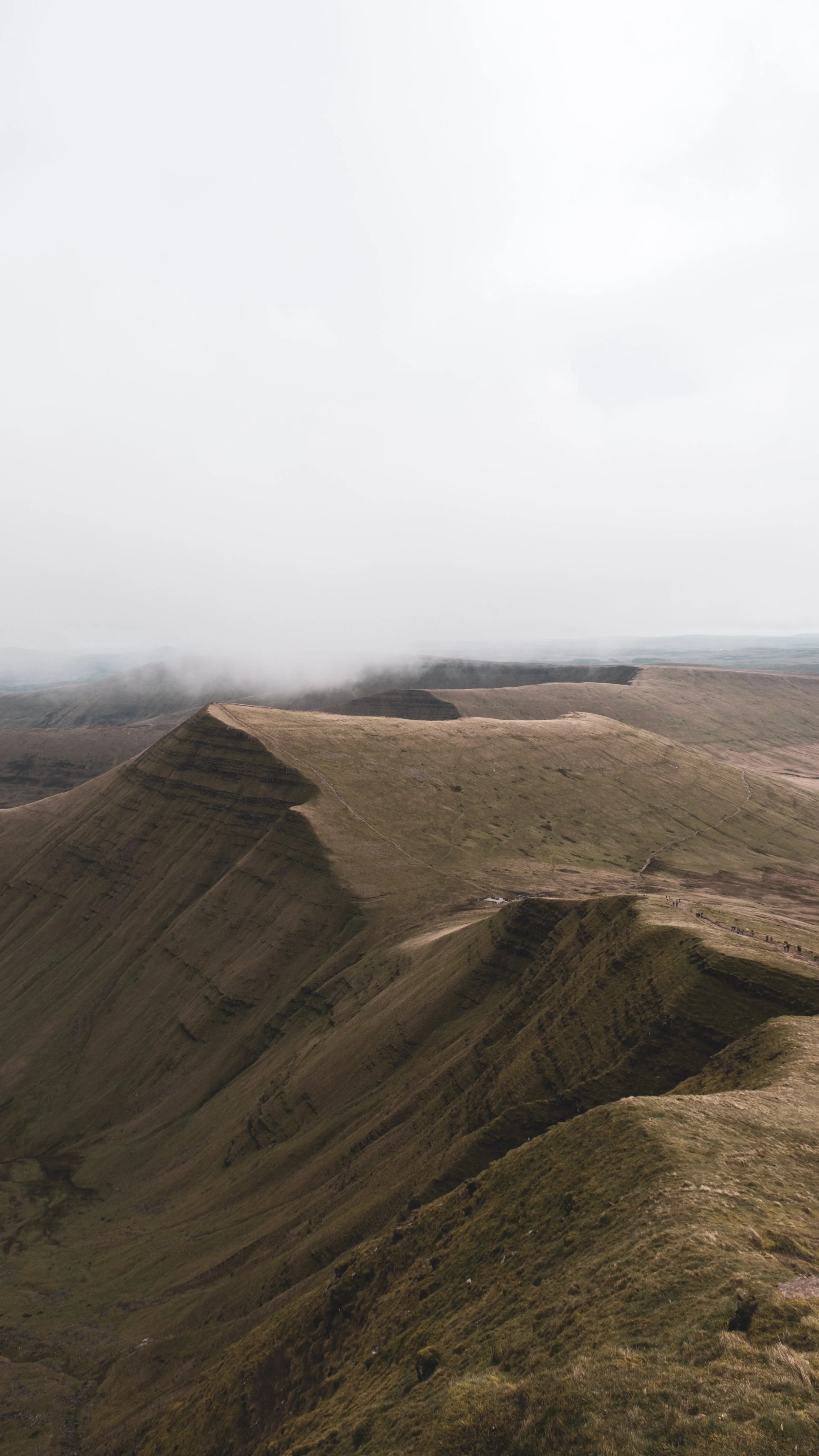 Hiking trail along the ridges of a grassy mountain on a cloudy day.