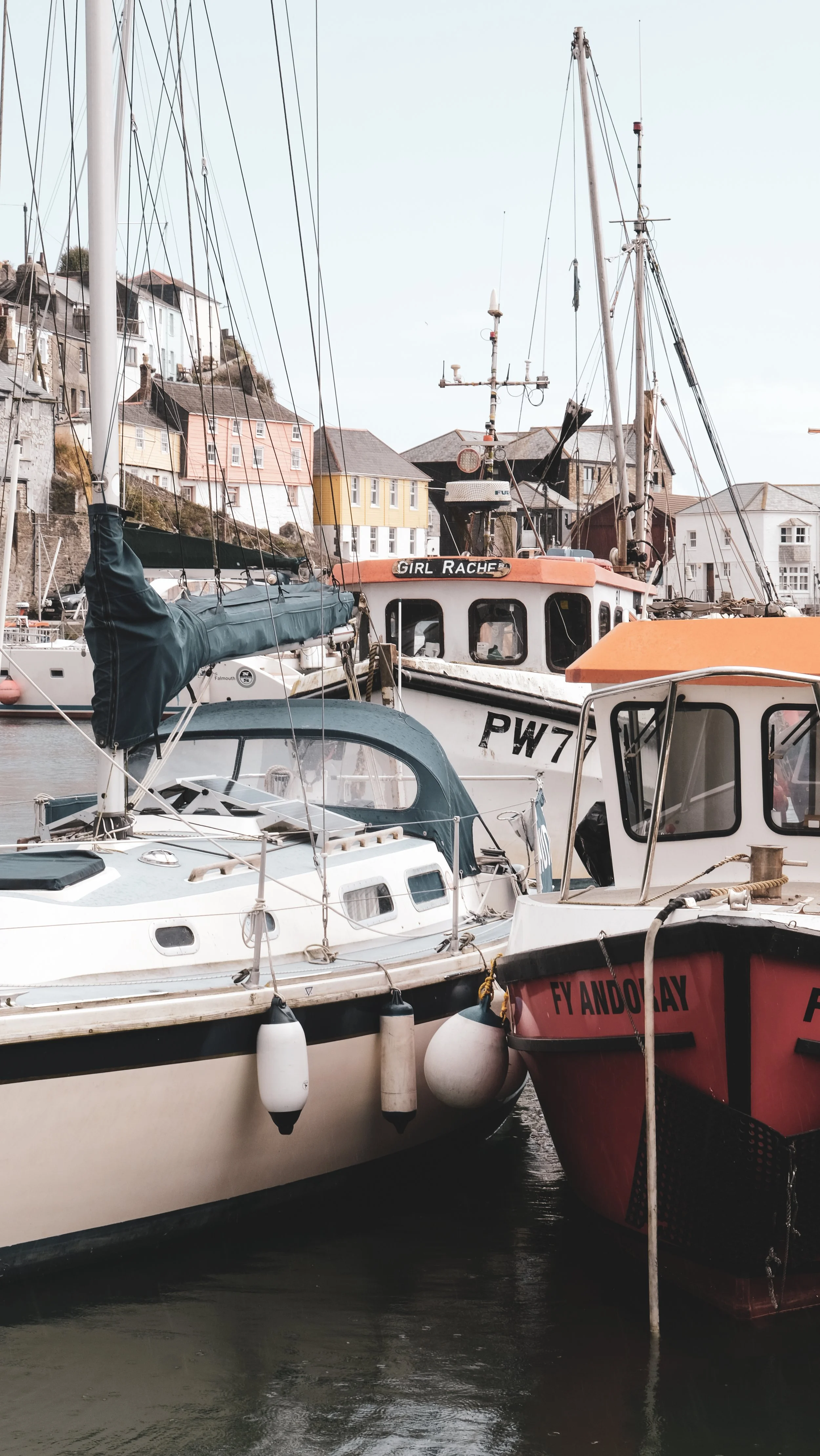 Multiple boats docked at a marina with colorful houses on a hillside in the background.