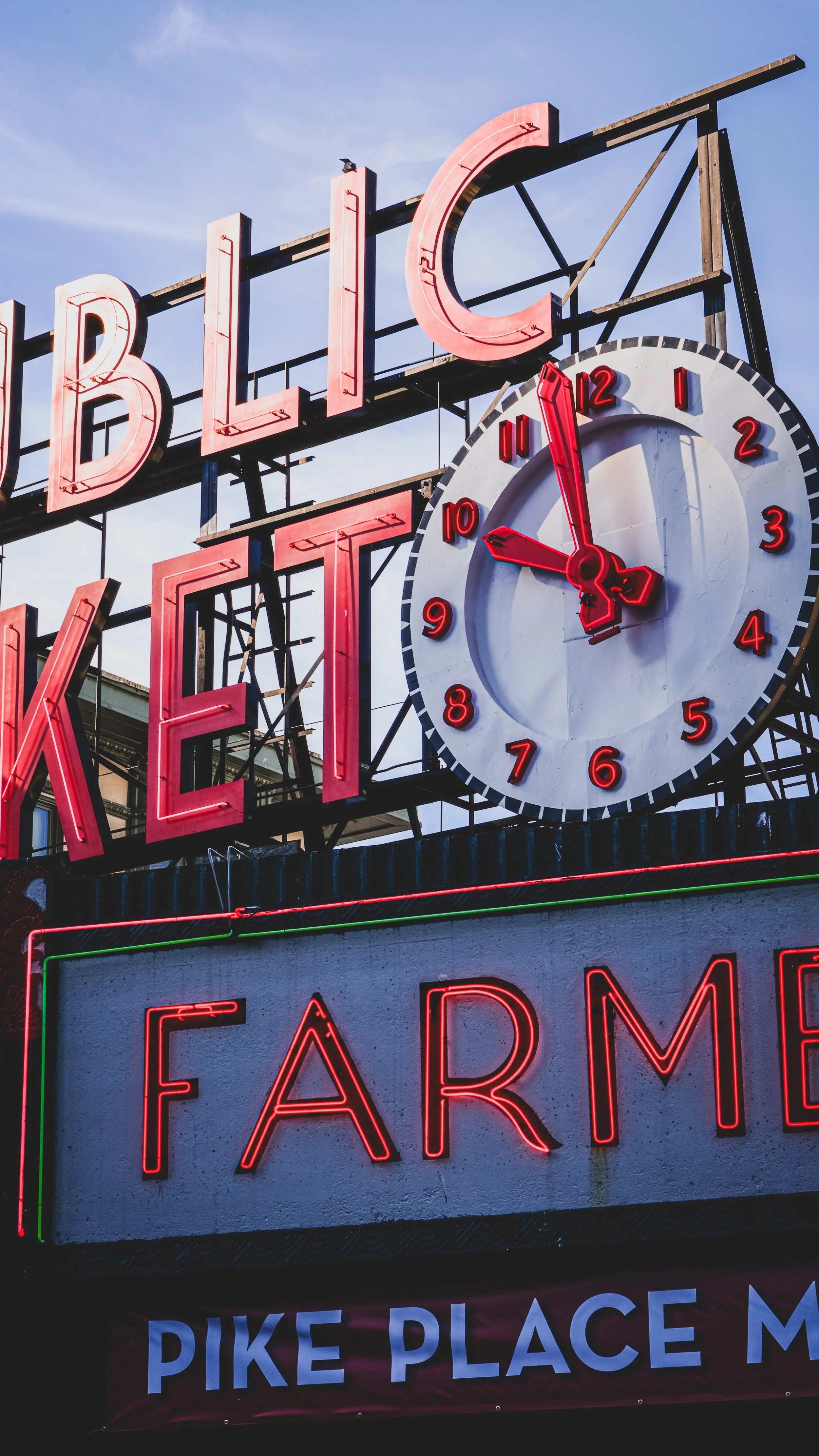 Neon sign showing the words 'Blue Jesse' with a large clock displaying 5:00, part of a sign for a farm, and a part of a banner that says 'Pike Place'.