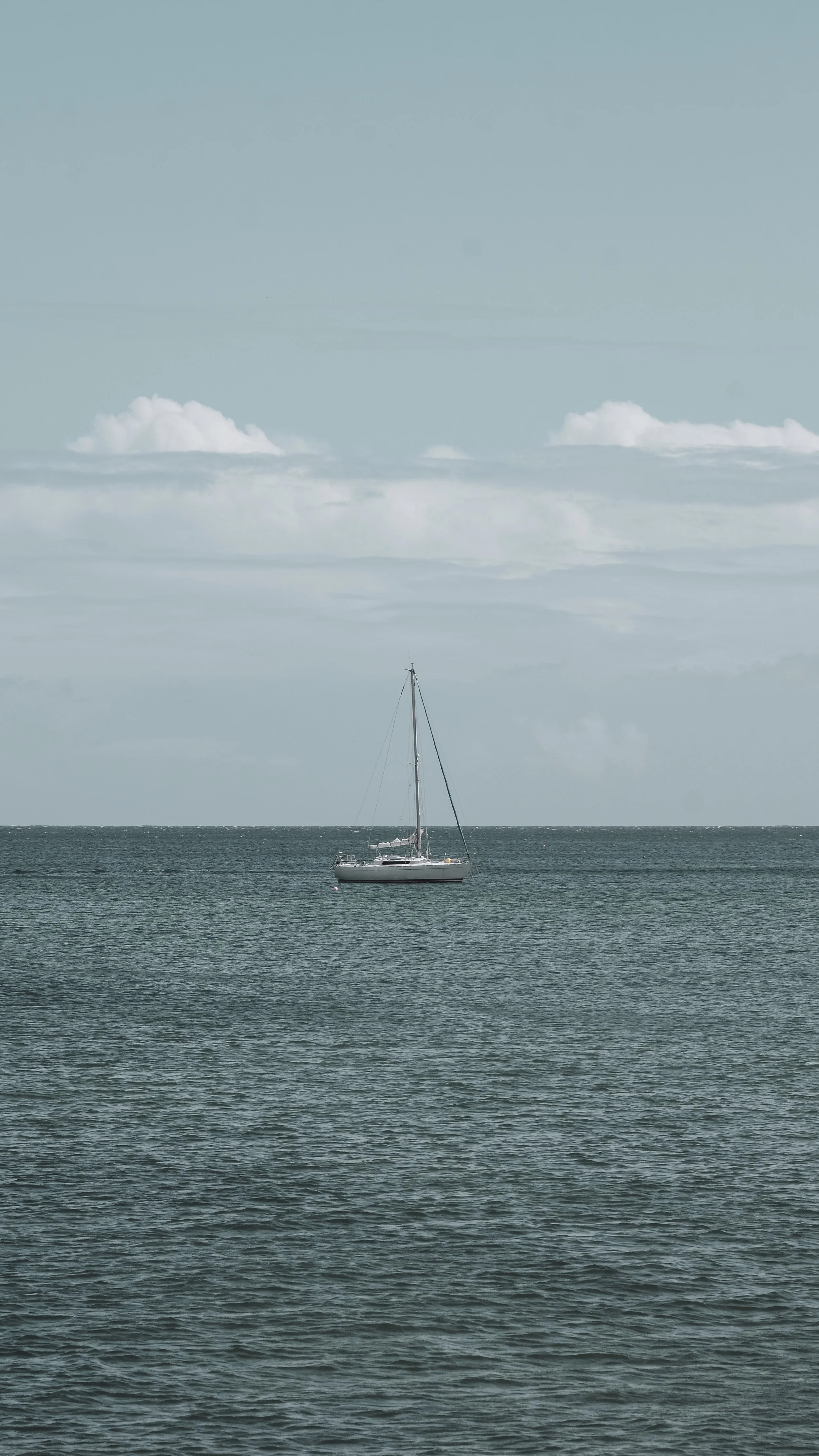 A sailboat floating on calm ocean waters with a cloudy sky in the background.