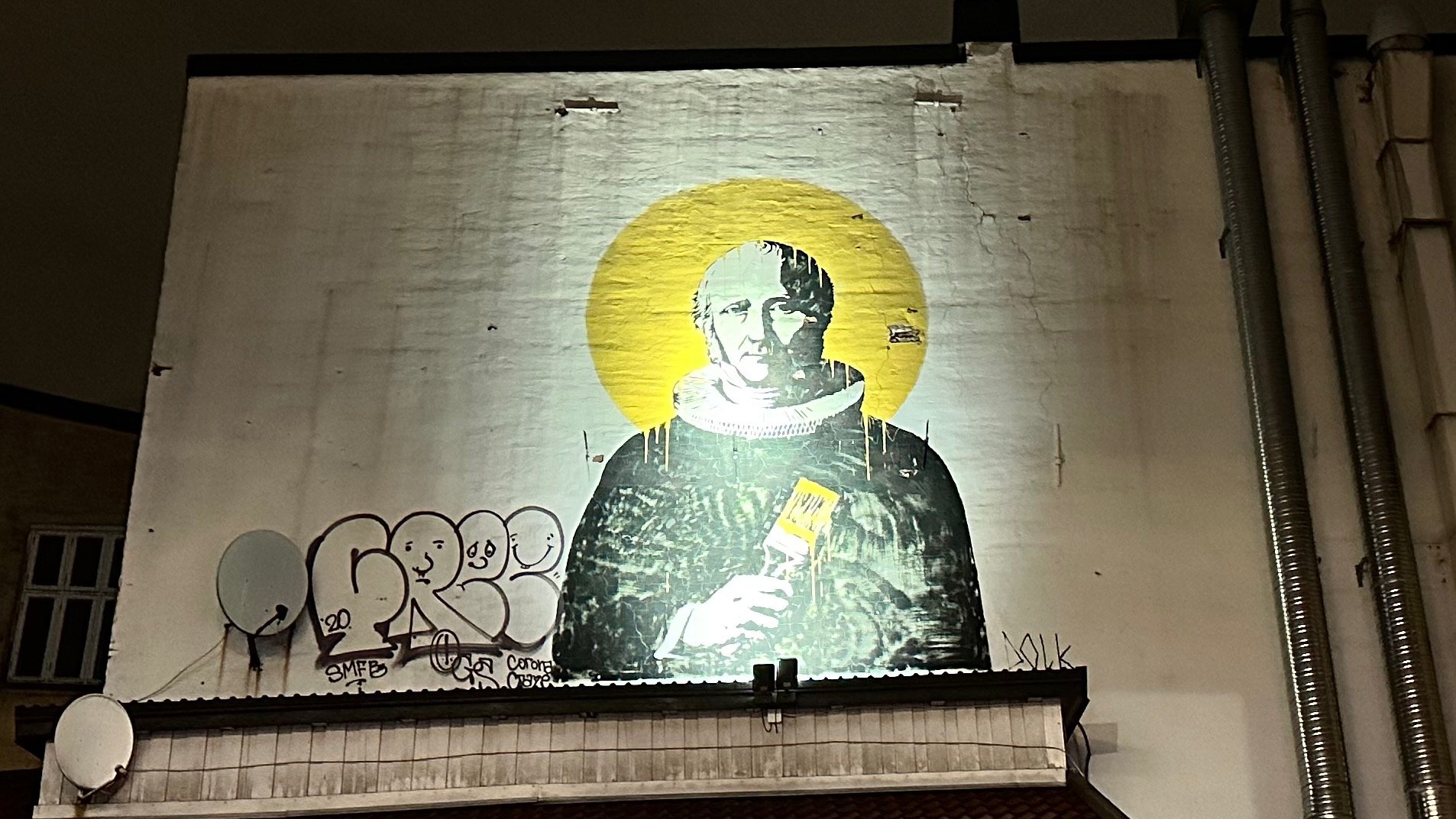 Street art mural of a person with a yellow halo, holding a paintbrush, on a building wall