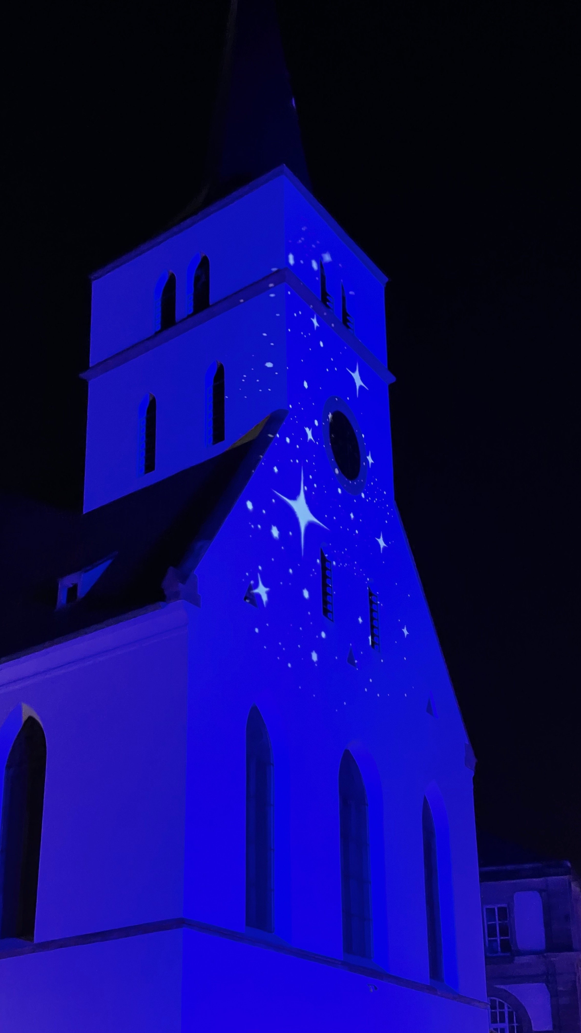 Church tower illuminated in blue with star projections at night.