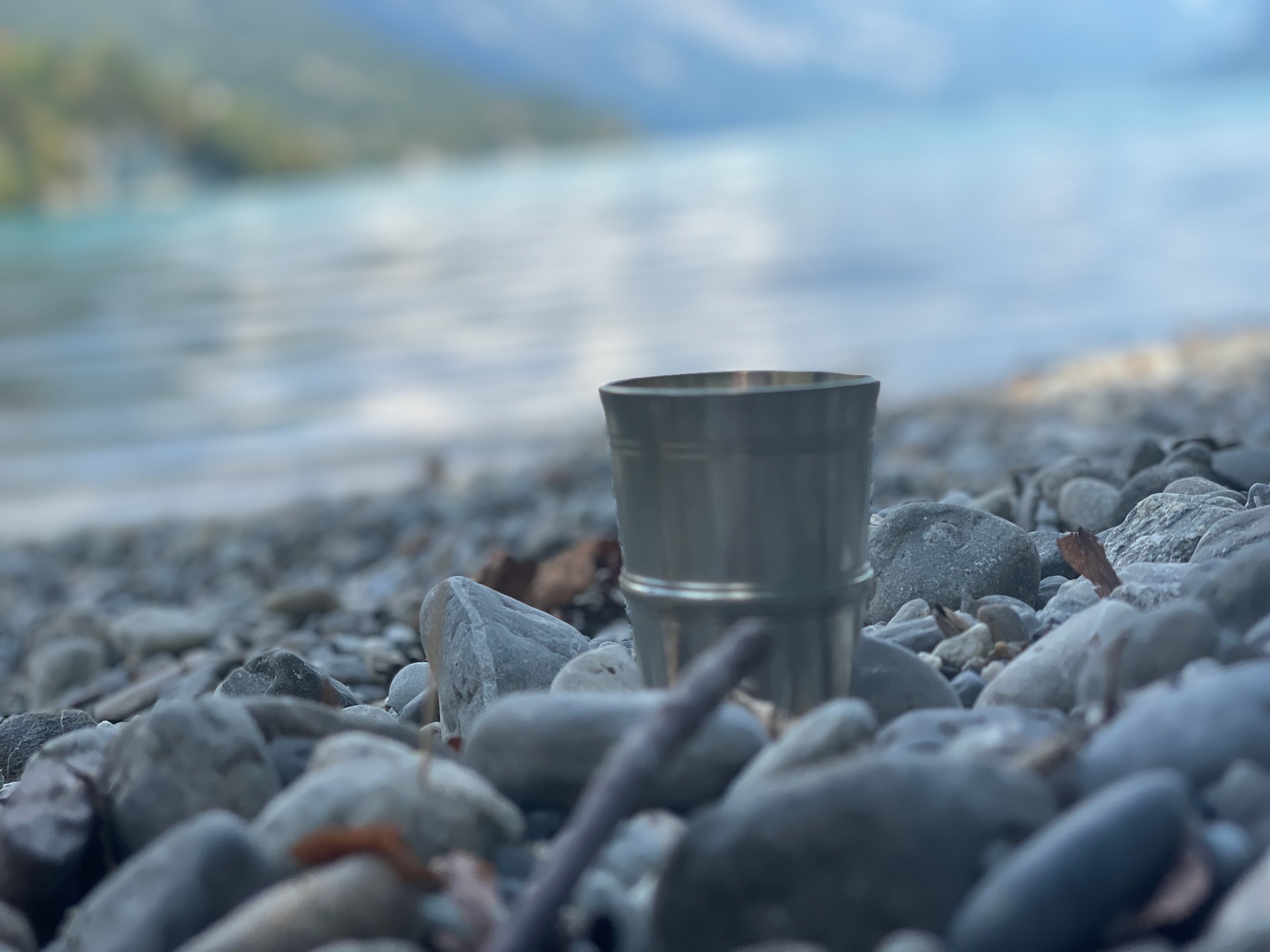 Metal cup on rocky lakeshore with blurred background