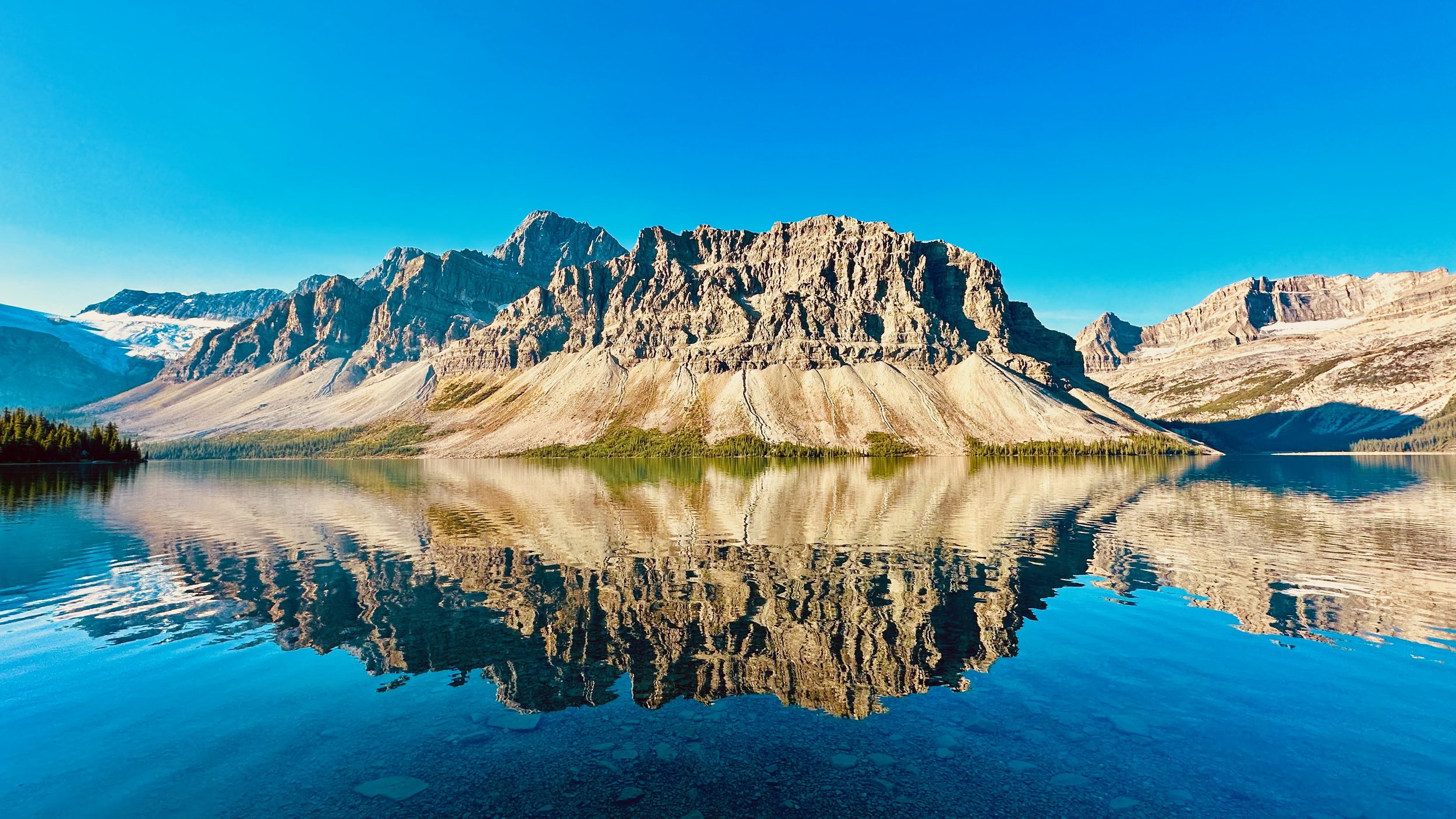 Mountain landscape with clear blue sky, rocky peaks, and a lake reflecting the mountains and sky.