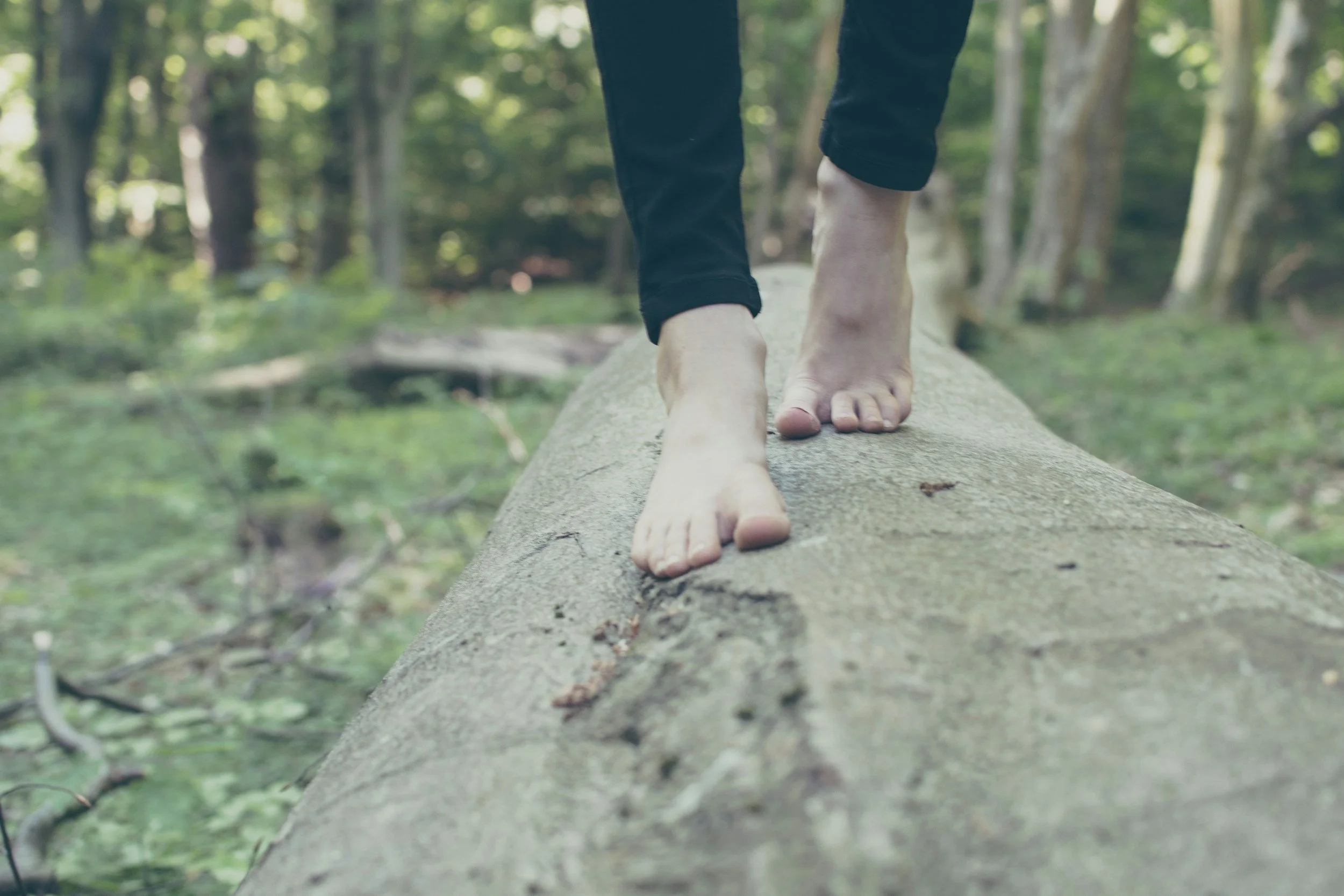 A person balancing on a tree log barefoot.