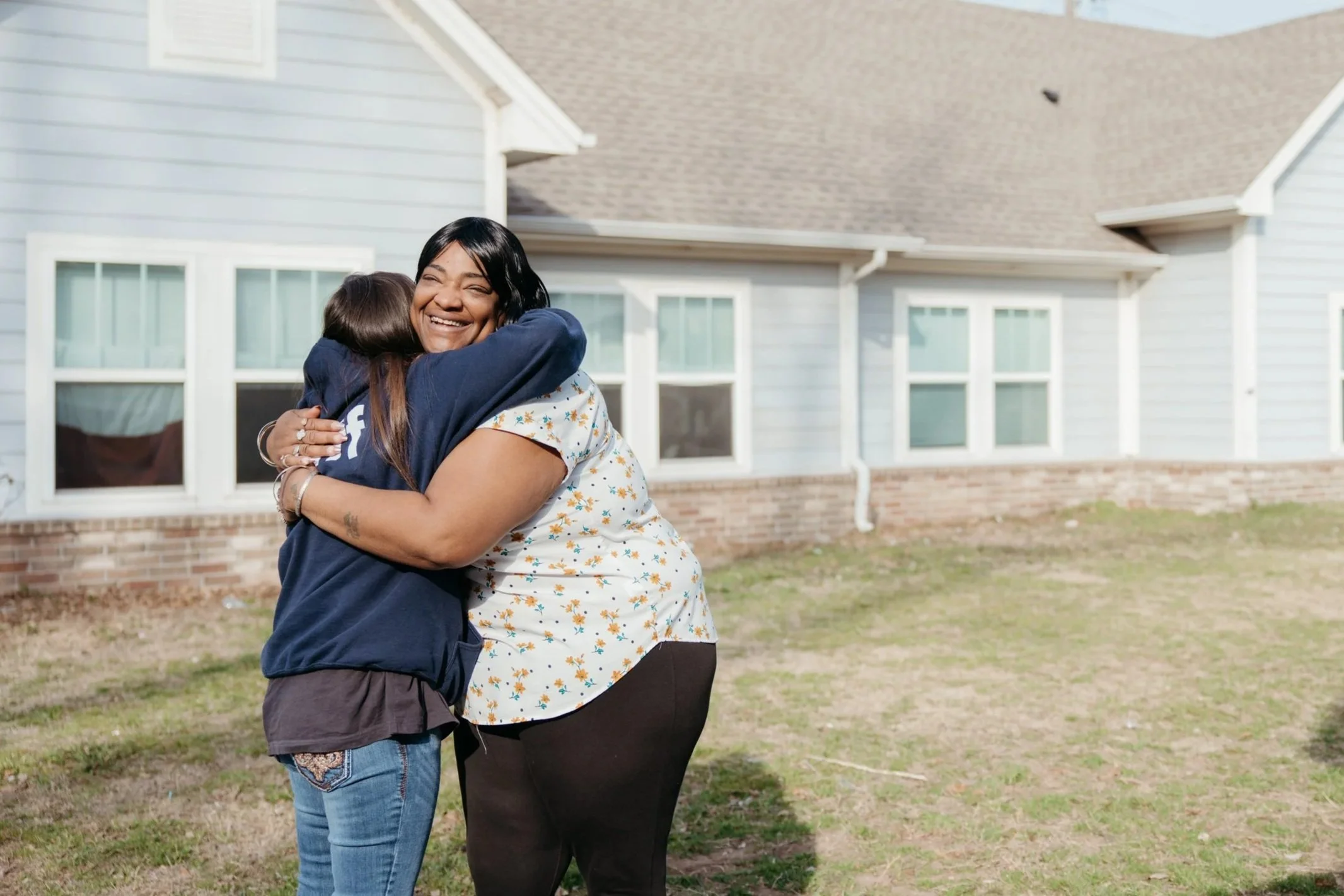 Two women hug and smile in front of City Care's supportive housing units.
