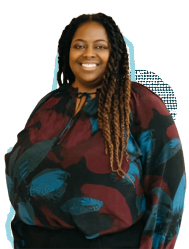 A woman with long, dark brown and blonde dreadlocks, smiling, wearing a colorfully patterned blouse with shades of maroon, blue, and black.