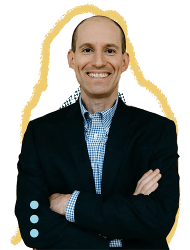 A smiling man in a navy blazer and blue checkered shirt with arms crossed, standing against a plain background.
