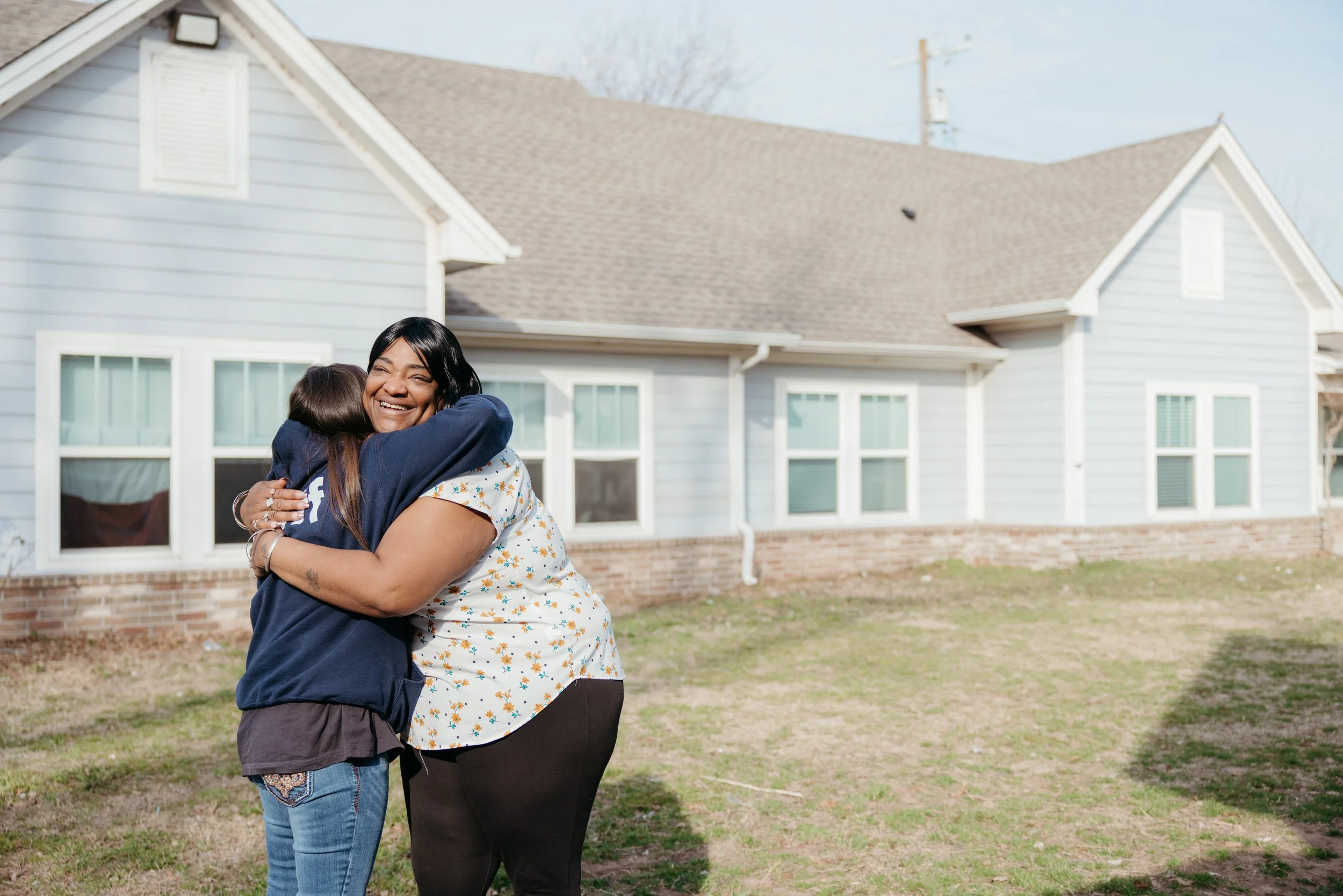 Two women hug in front of a house that is one of City Care's supportive housing units