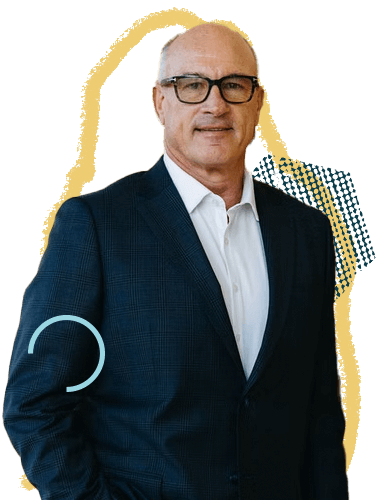 A man in a dark suit and white shirt, wearing glasses, standing against a colorful abstract background.