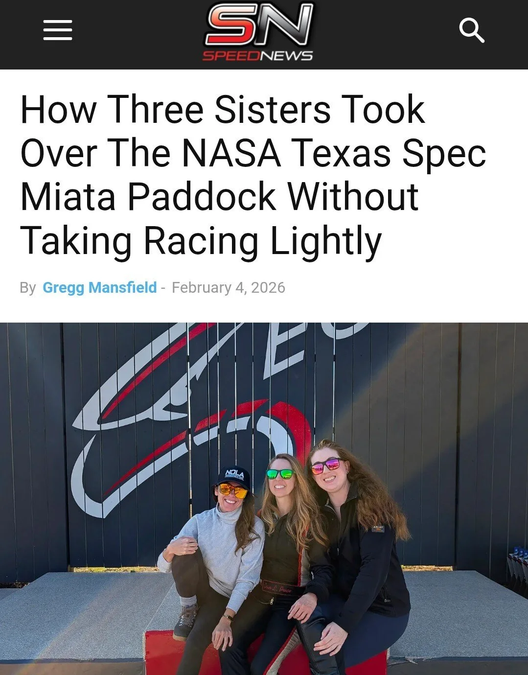 Three women sitting in front of a black wall with a large red and white logo, smiling and wearing sunglasses